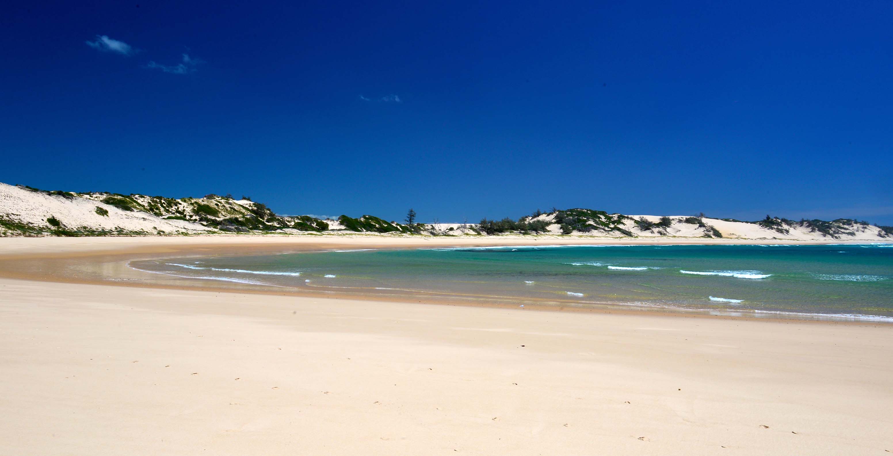 Deserted beach on Bazaruto Island forming small bay, white sand, crystal blue sea