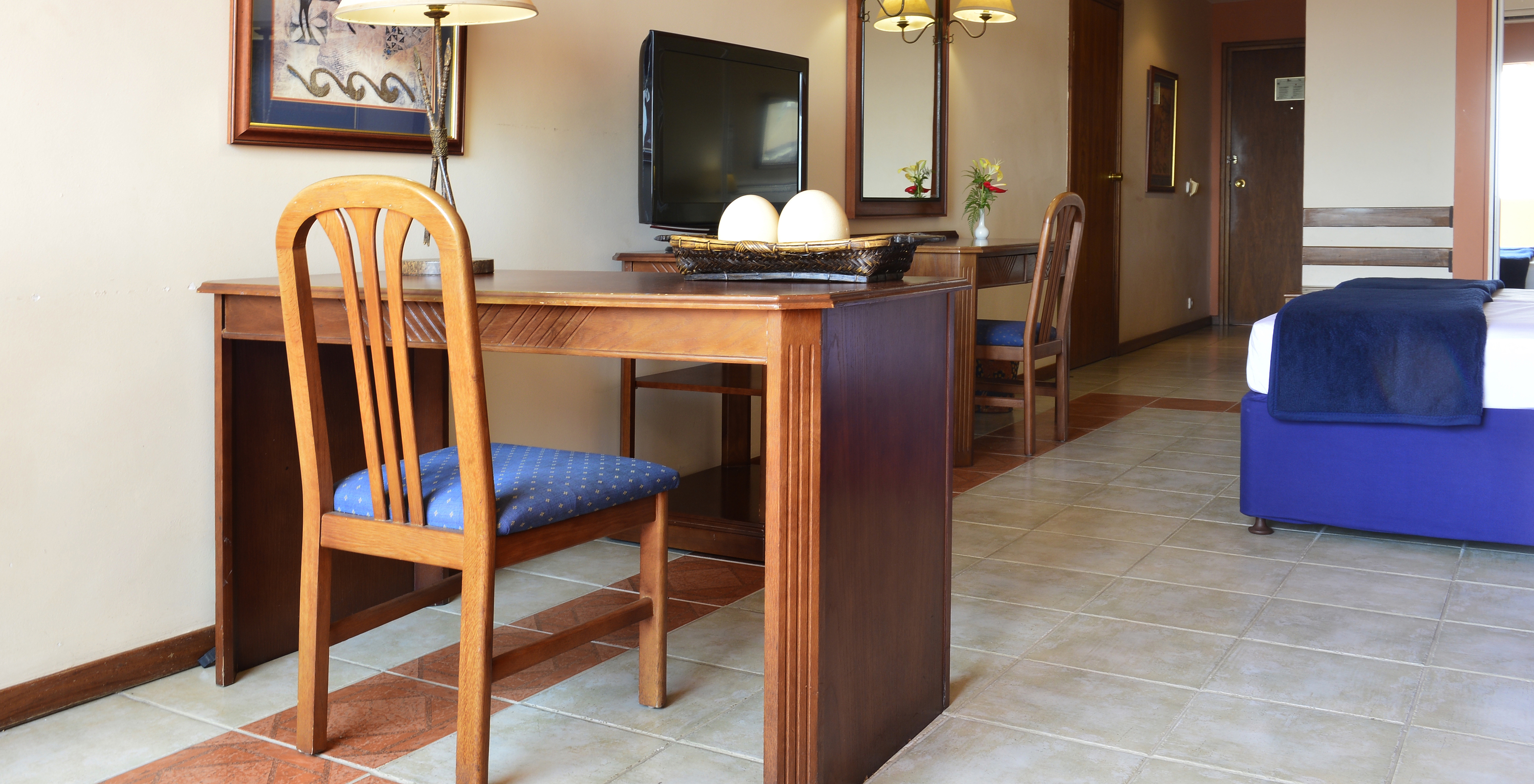 The Family Executive Suite of Pestana Rovuma has a desk and wooden chair, with a lamp and a picture