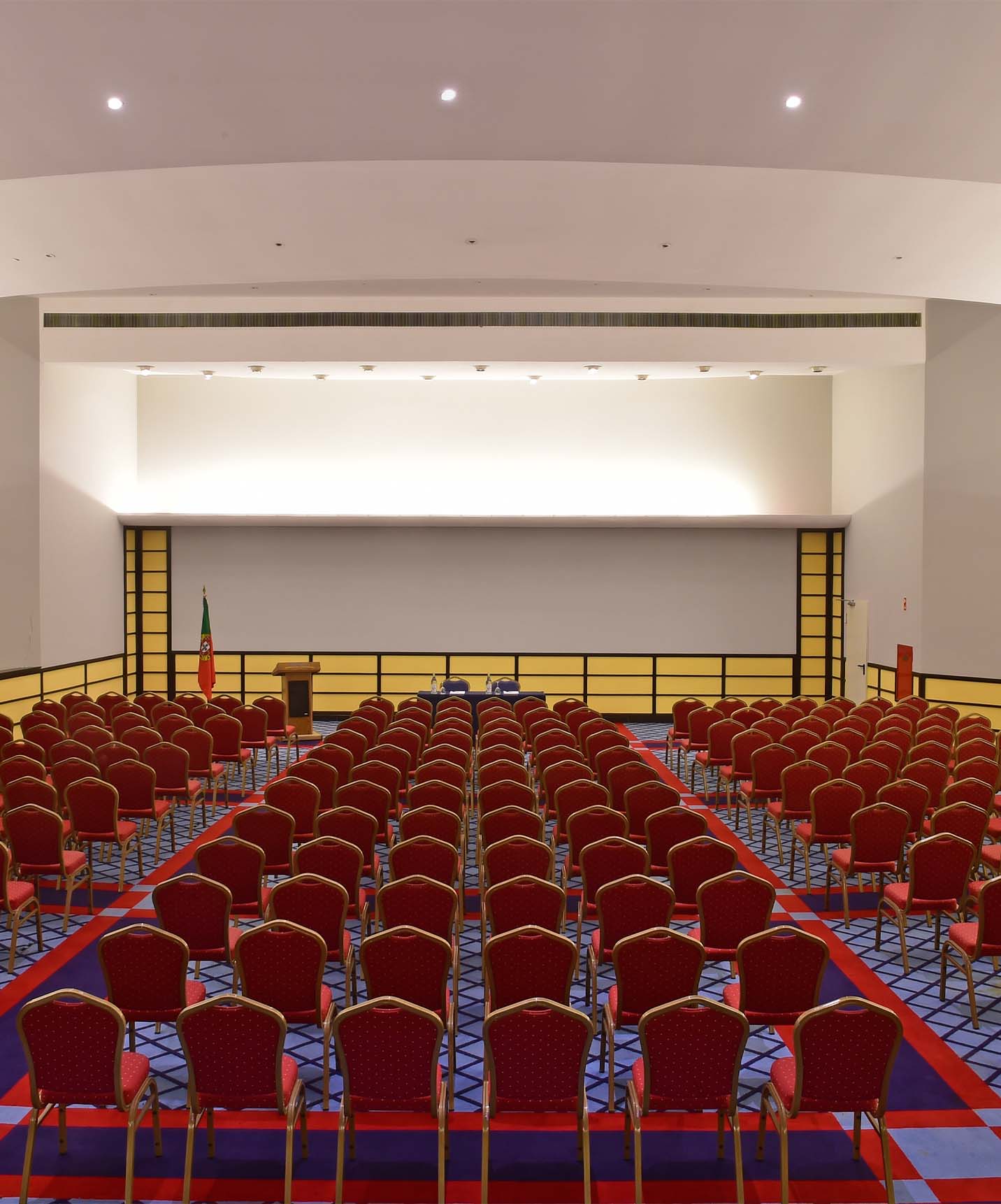 Amphitheater with red chairs and blue and red carpet, Portuguese flag, yellow walls, and white ceiling