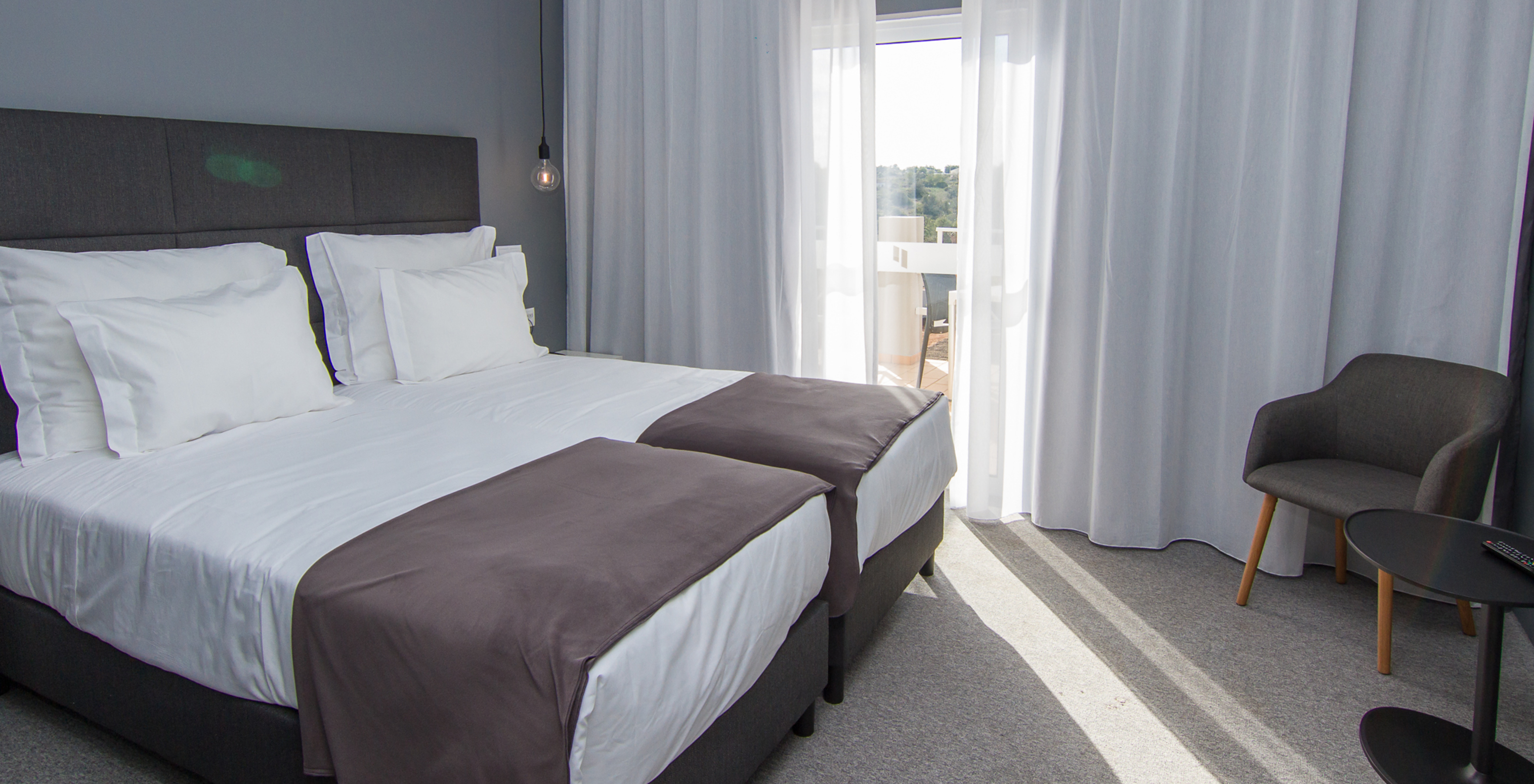 The Classic Pool View room at Pestana Gramacho Residences features two single beds, a chair, and a window