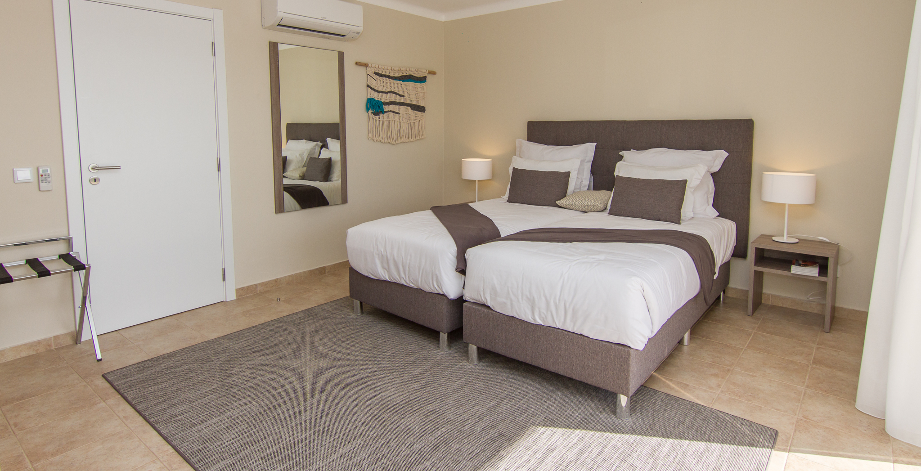 The T1 Apartment at Pestana Gramacho Residences has a white door, two beds, two bedside tables, and air conditioning