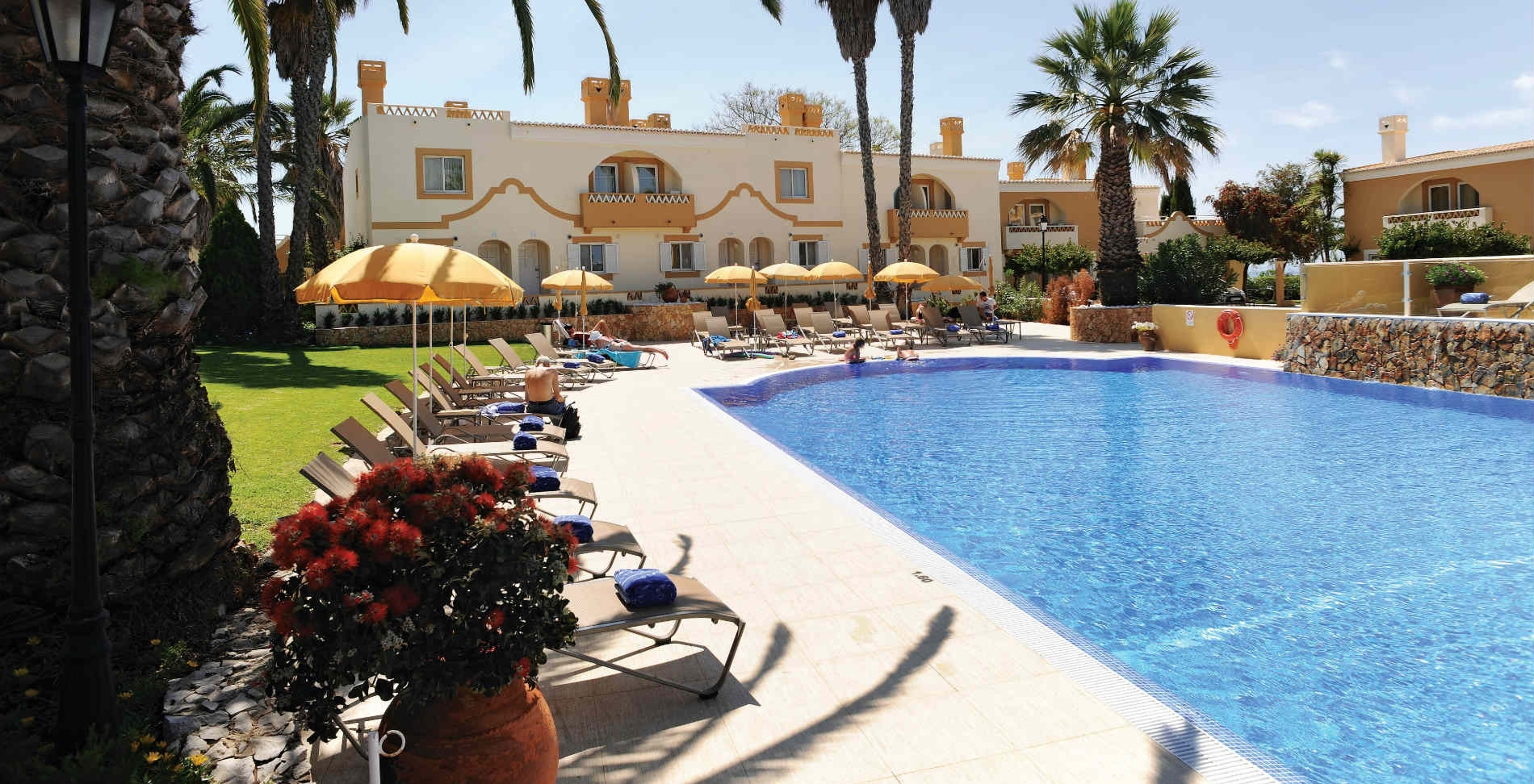 Outdoor pool at Pestana Palm Gardens with sun loungers, several people sunbathing or under umbrellas