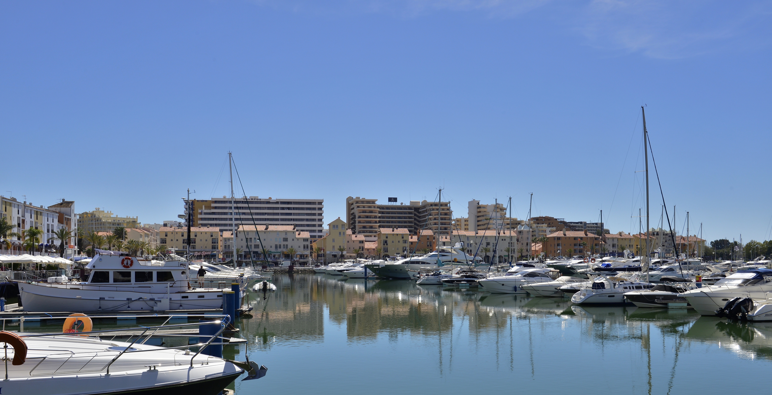 Vilamoura Marina in Algarve on a sunny day with blue skies, anchored boats, and water reflecting distant buildings