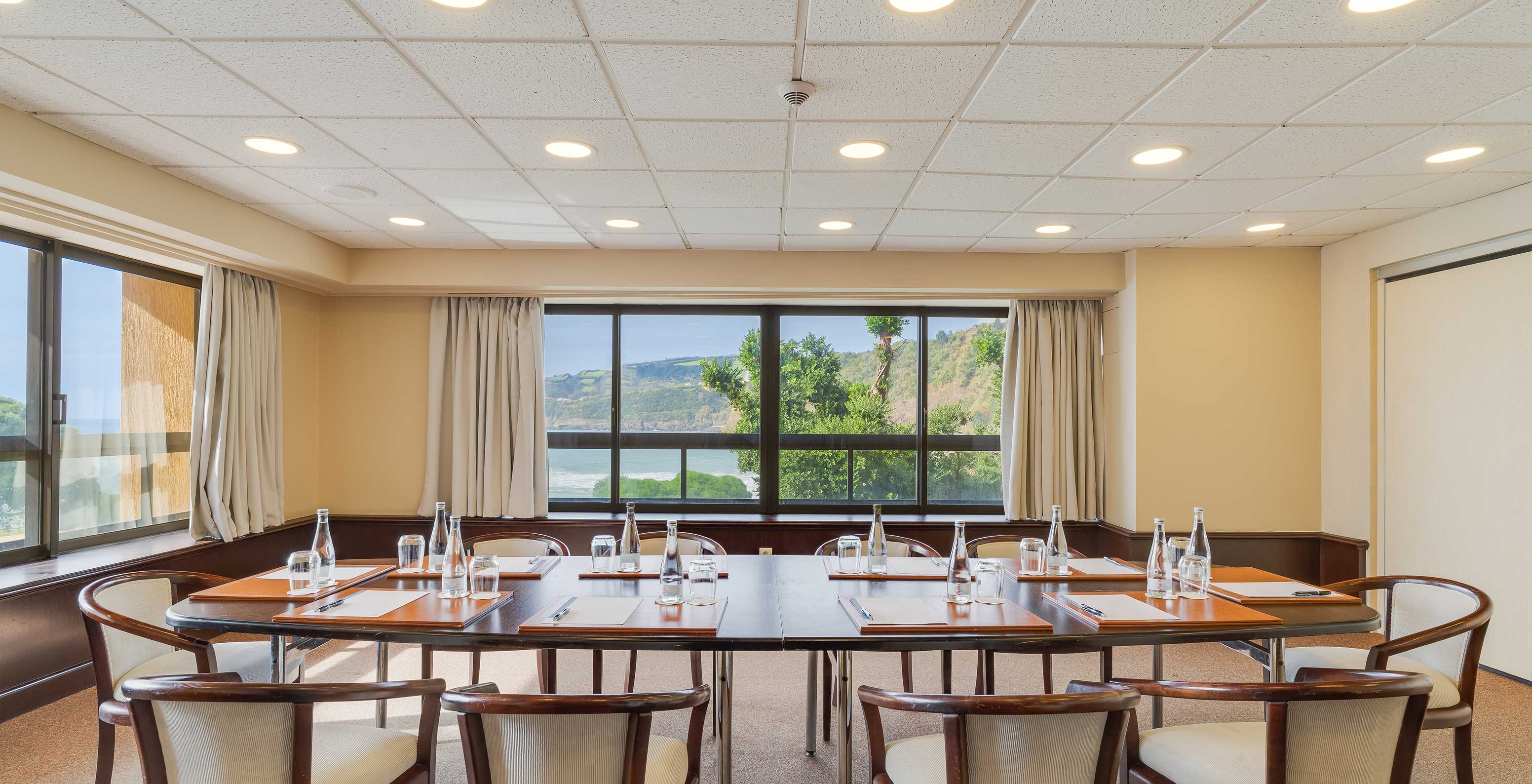 The hotel on São Miguel Island has meeting rooms with tables and chairs set up, with a sea and nature view