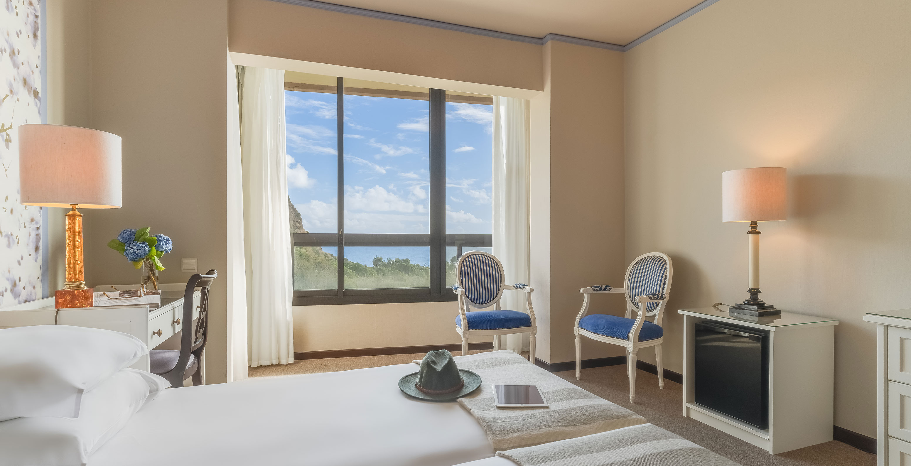 Standard Garden View room at Pestana Bahia Praia has two chairs near the window with a view of the green island landscape