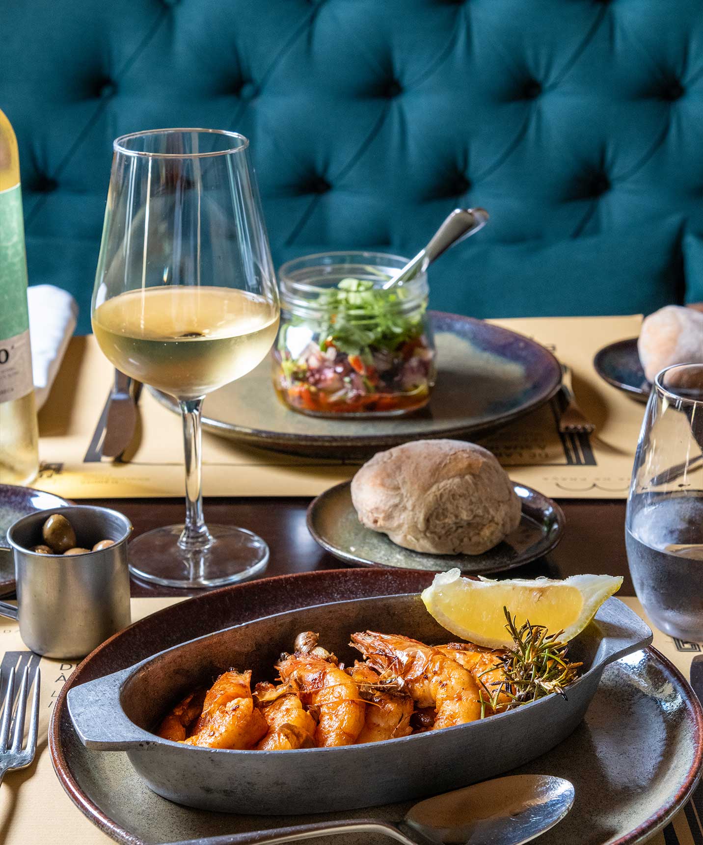 Table with a plate of shrimp, salad, and a glass of white wine at a hotel with spa and pool overlooking the sea