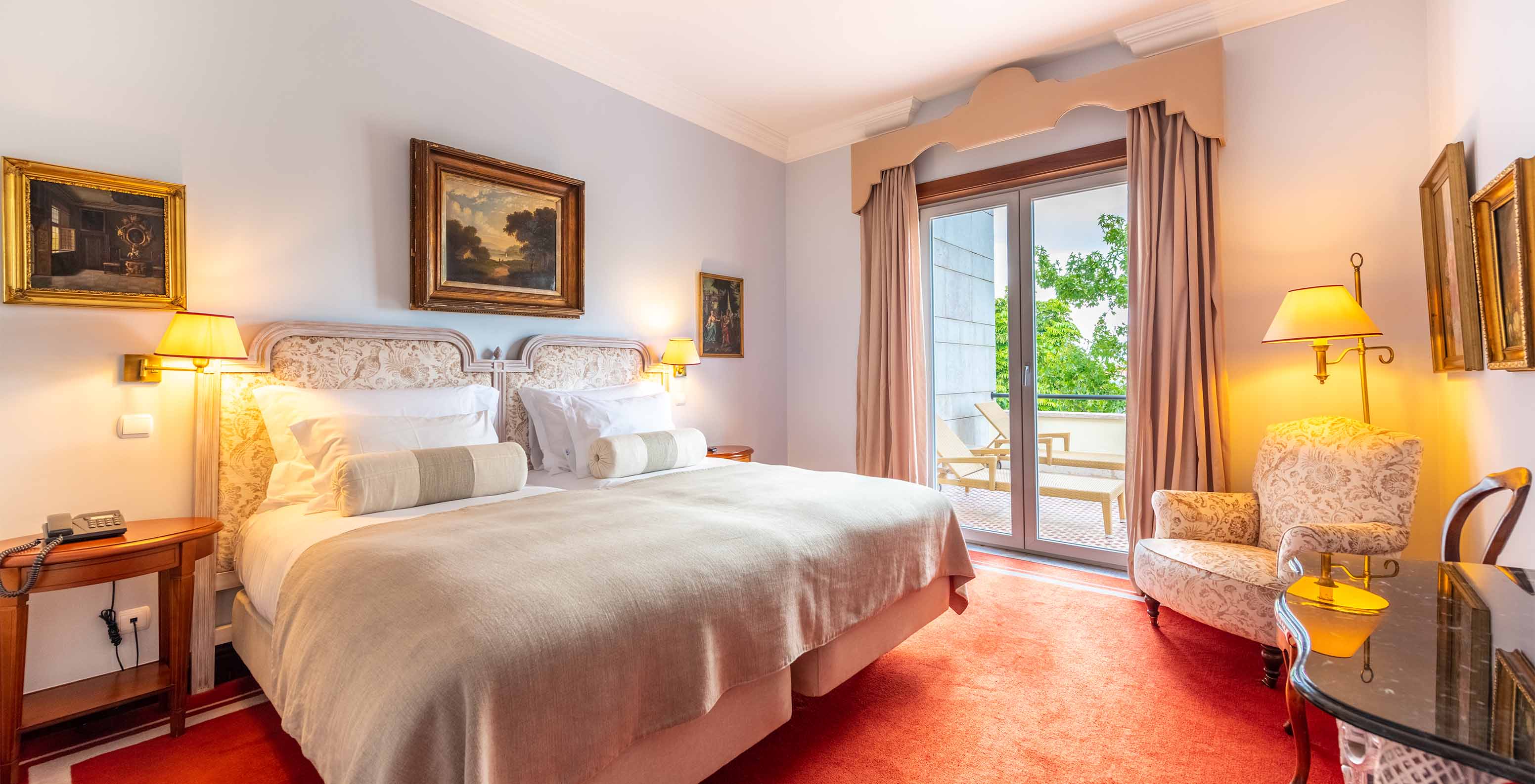 The Suite Collection at Pestana Palace Lisbon has a double bed, an armchair, a desk, and a window with access to the garden