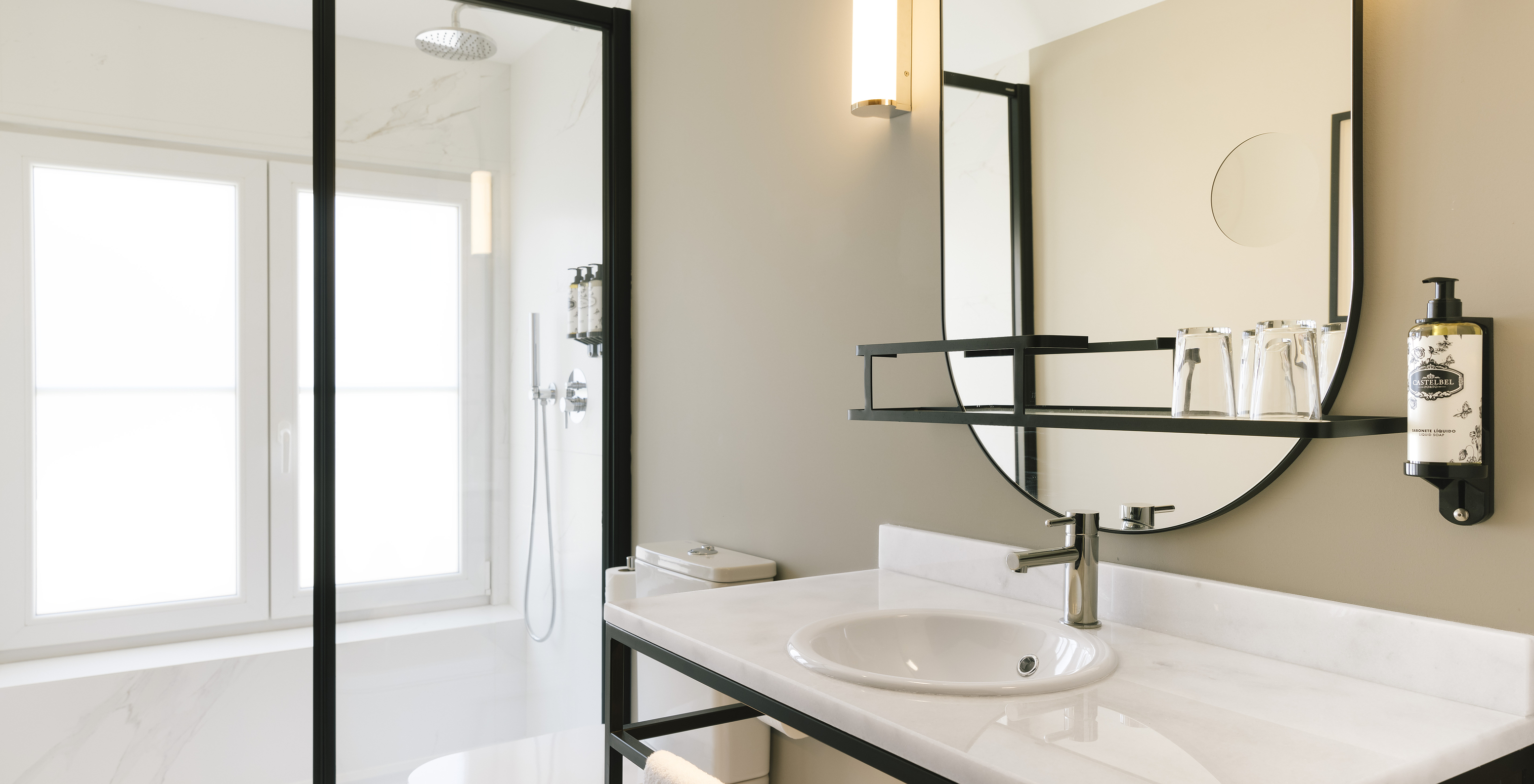 The Junior Suite of Pestana Rua Augusta Lisboa has a bathroom with white marble sink, mirror, toilet, and shower