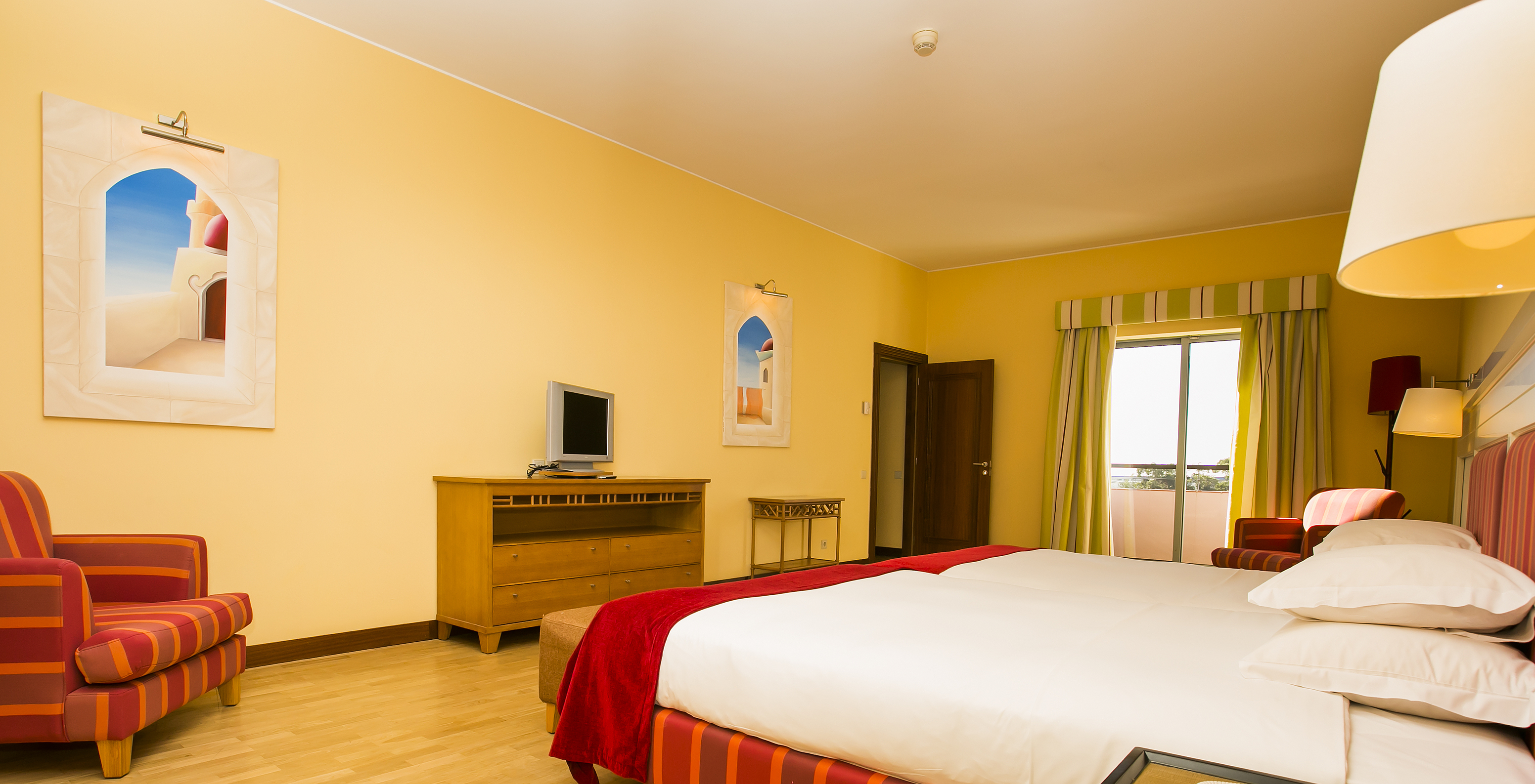 The Deluxe Mezzanine Suite of Pestana Sintra Golf has two beds, a small television, and a window with balcony access