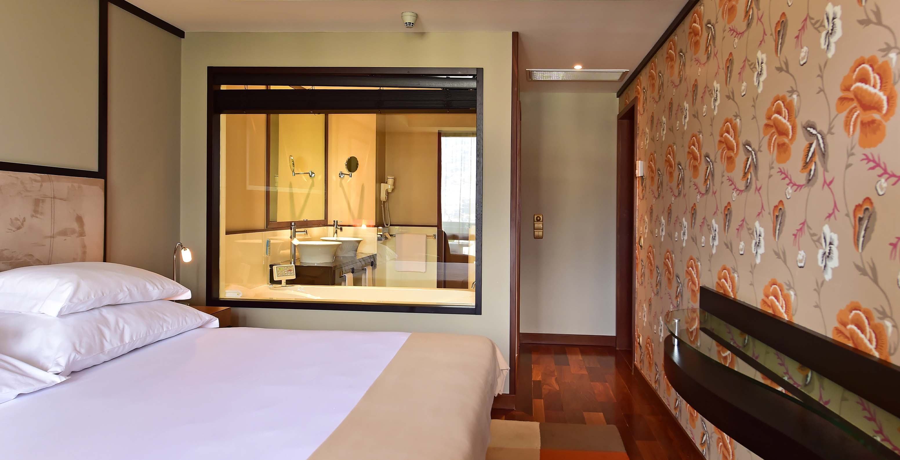 The Presidential Suite at Pestana Casino Park has a double bed with glass to the bathroom and decorative wallpaper