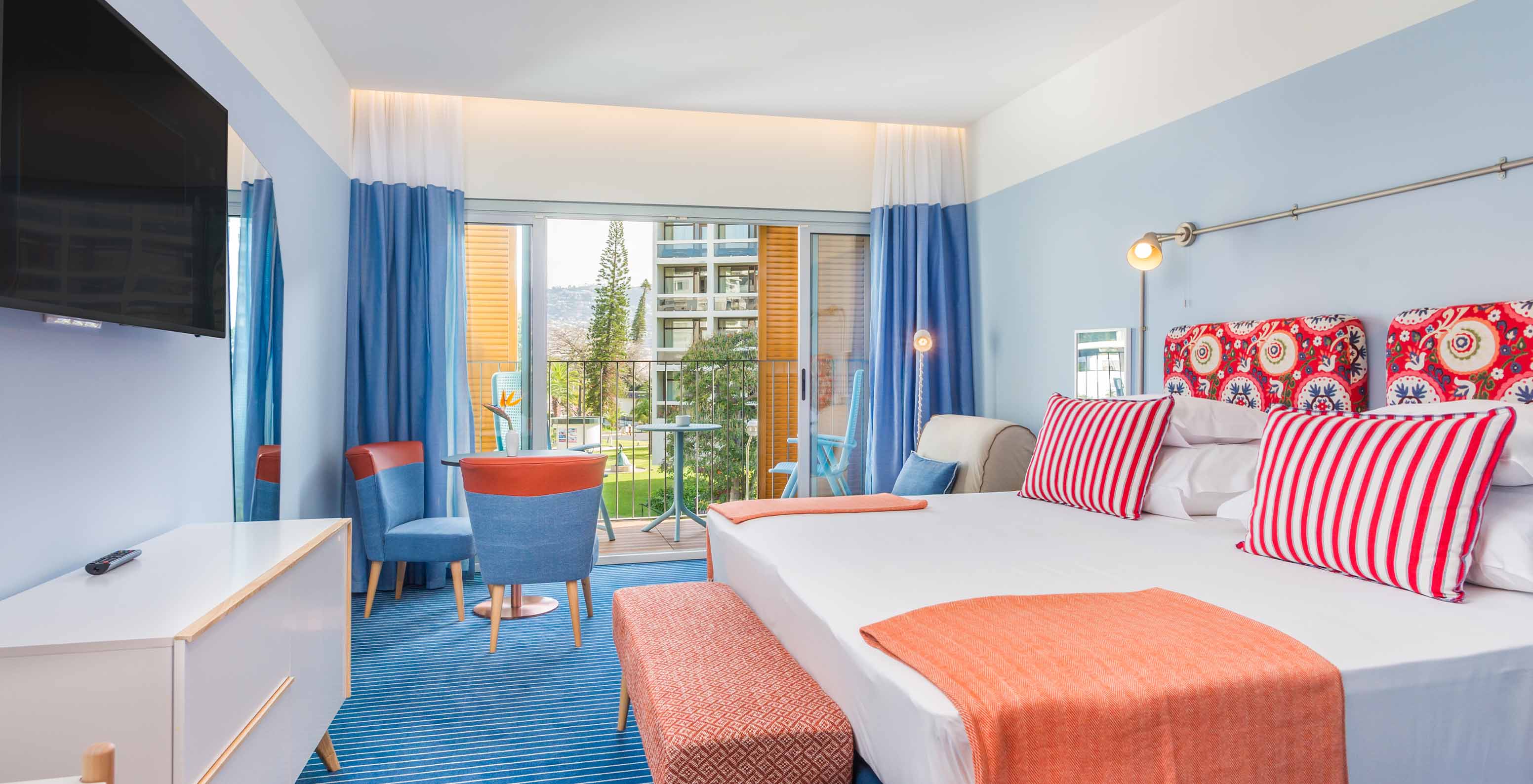 The Deluxe Studio at Pestana Casino Studios has a double bed with a patterned headboard, a balcony, and a TV