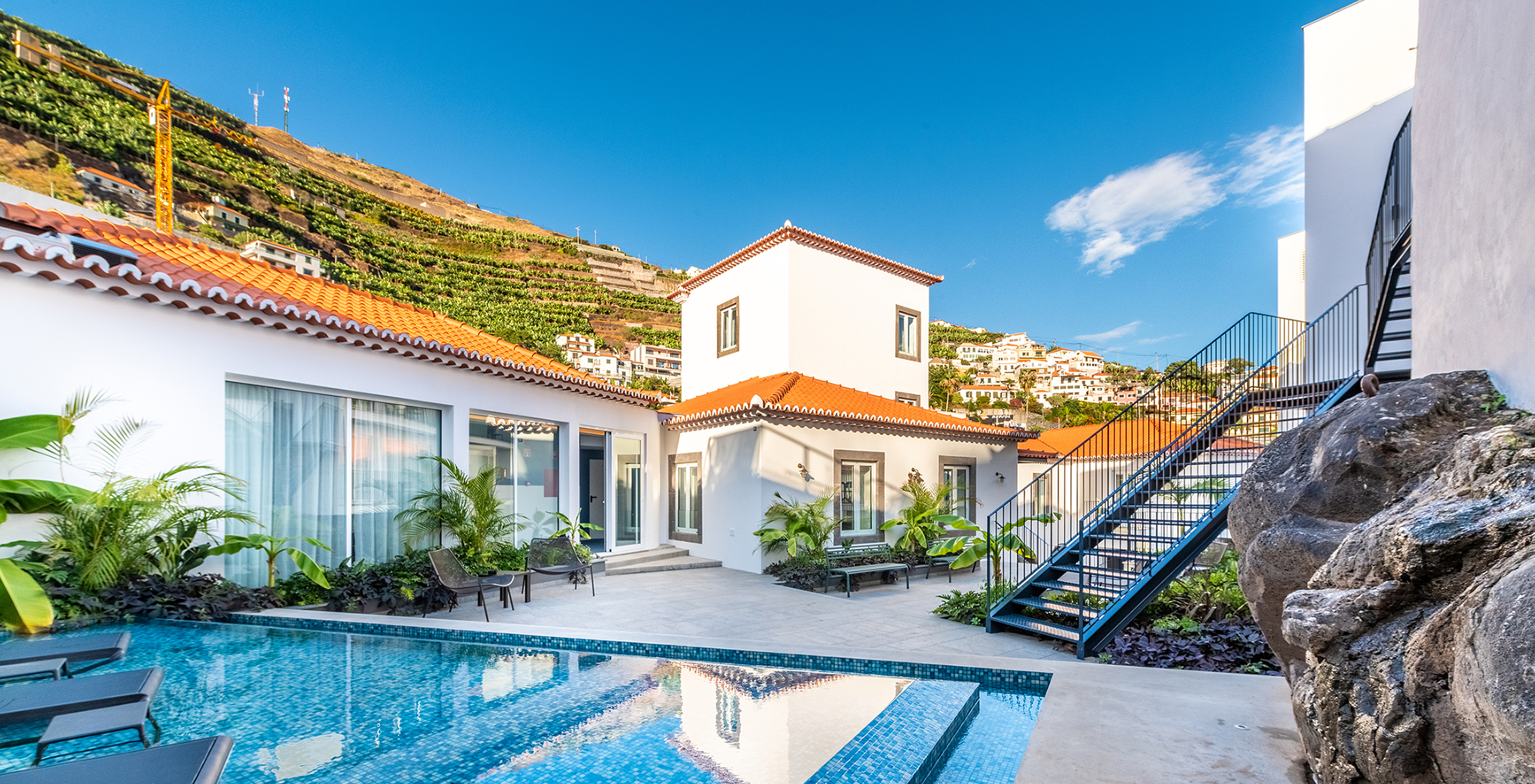 Hotel pool in Câmara de Lobos, Madeira, with loungers in water, plants, and benches