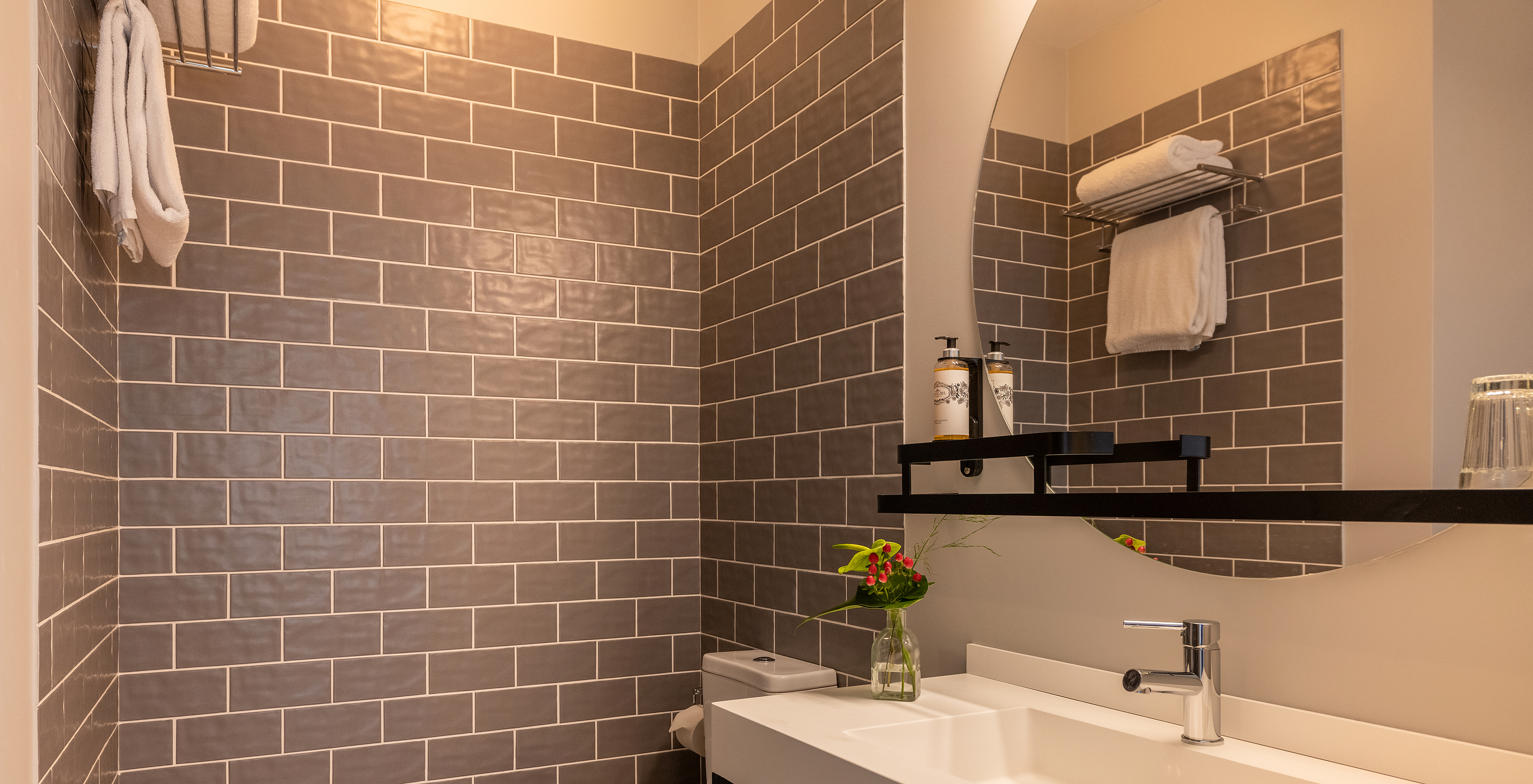 The Cozy room at Pestana Fisherman Village features a bathroom with gray tiles, a toilet, and a round mirror