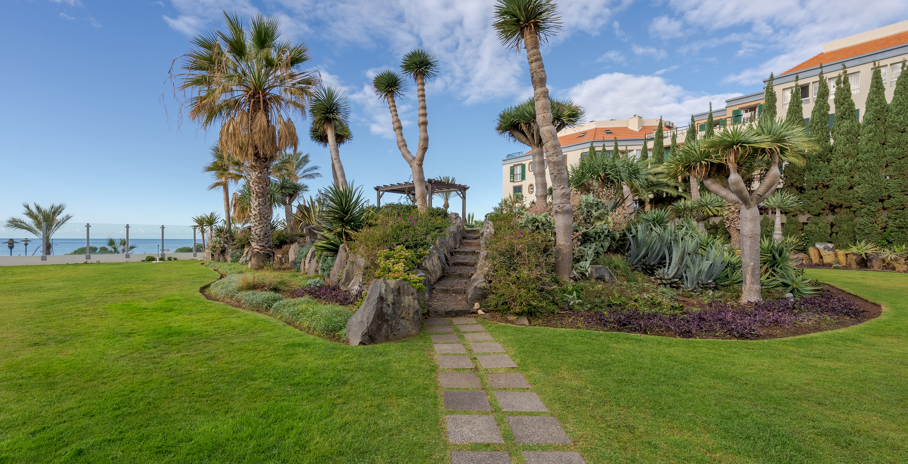 Lush garden landscape with various plants, manicured green grass, and a sea view