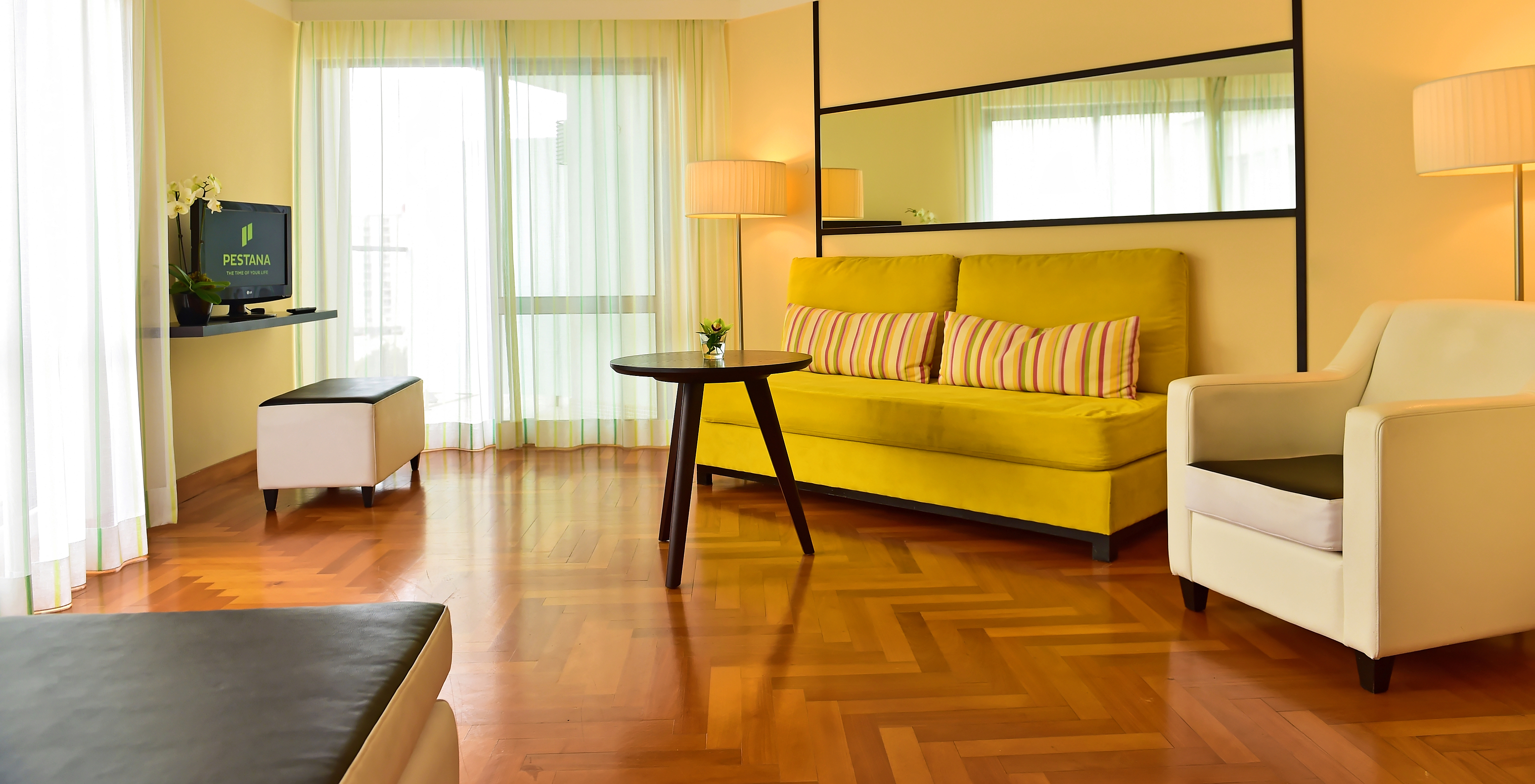 The Classic of Pestana Promenade has a living room with a green sofa, an armchair, and a television on a shelf