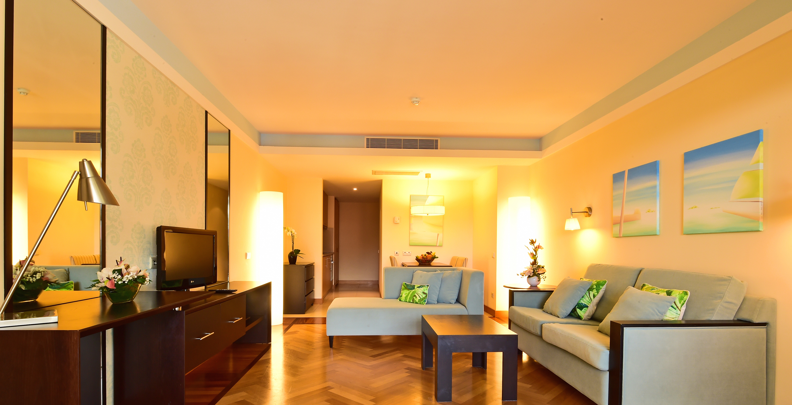 The Suite of Pestana Promenade has a living room with two sofas, a television, mirrors, and hanging paintings