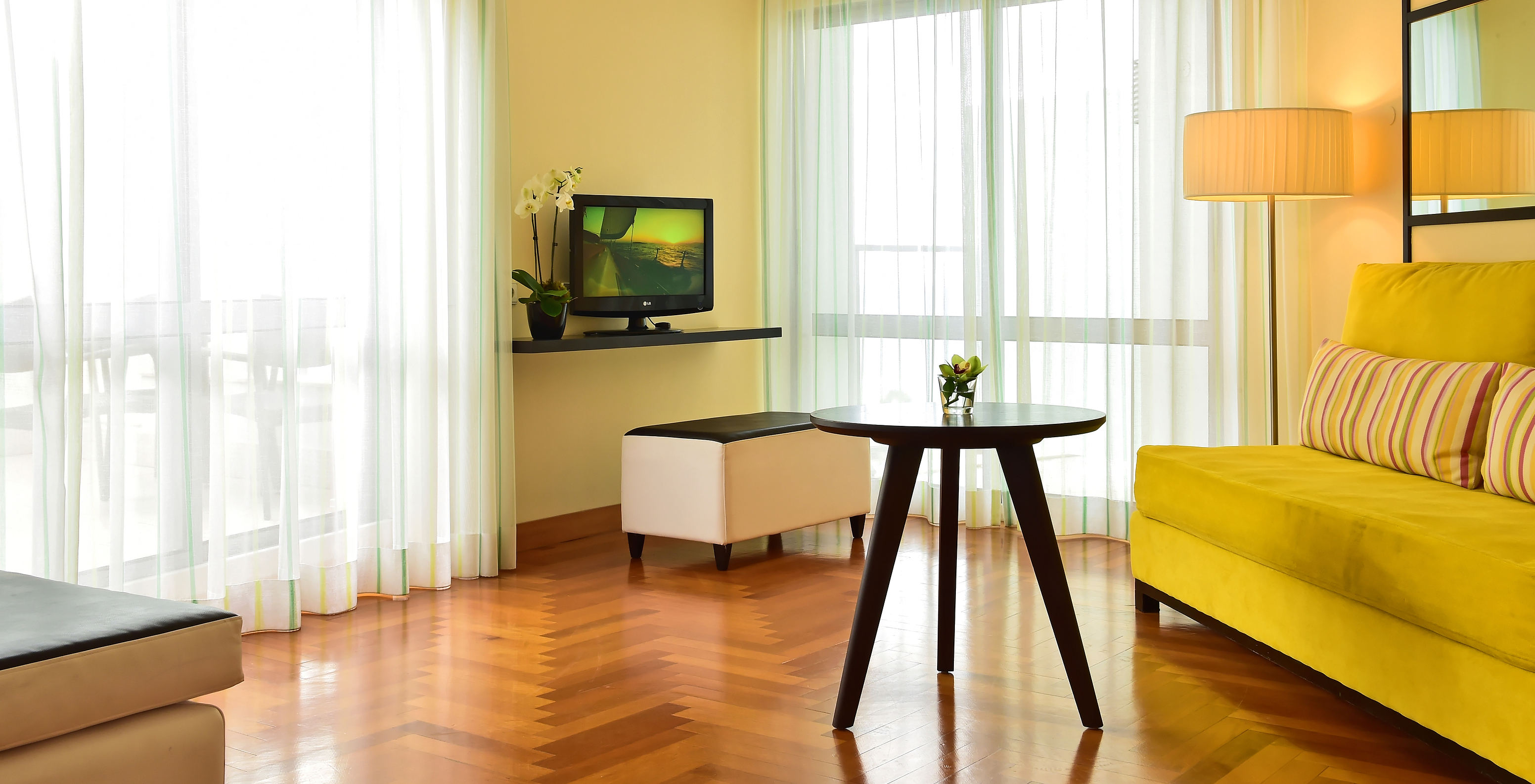 The Junior Suite of Pestana Promenade has a living room with a green sofa, a television, and two large windows