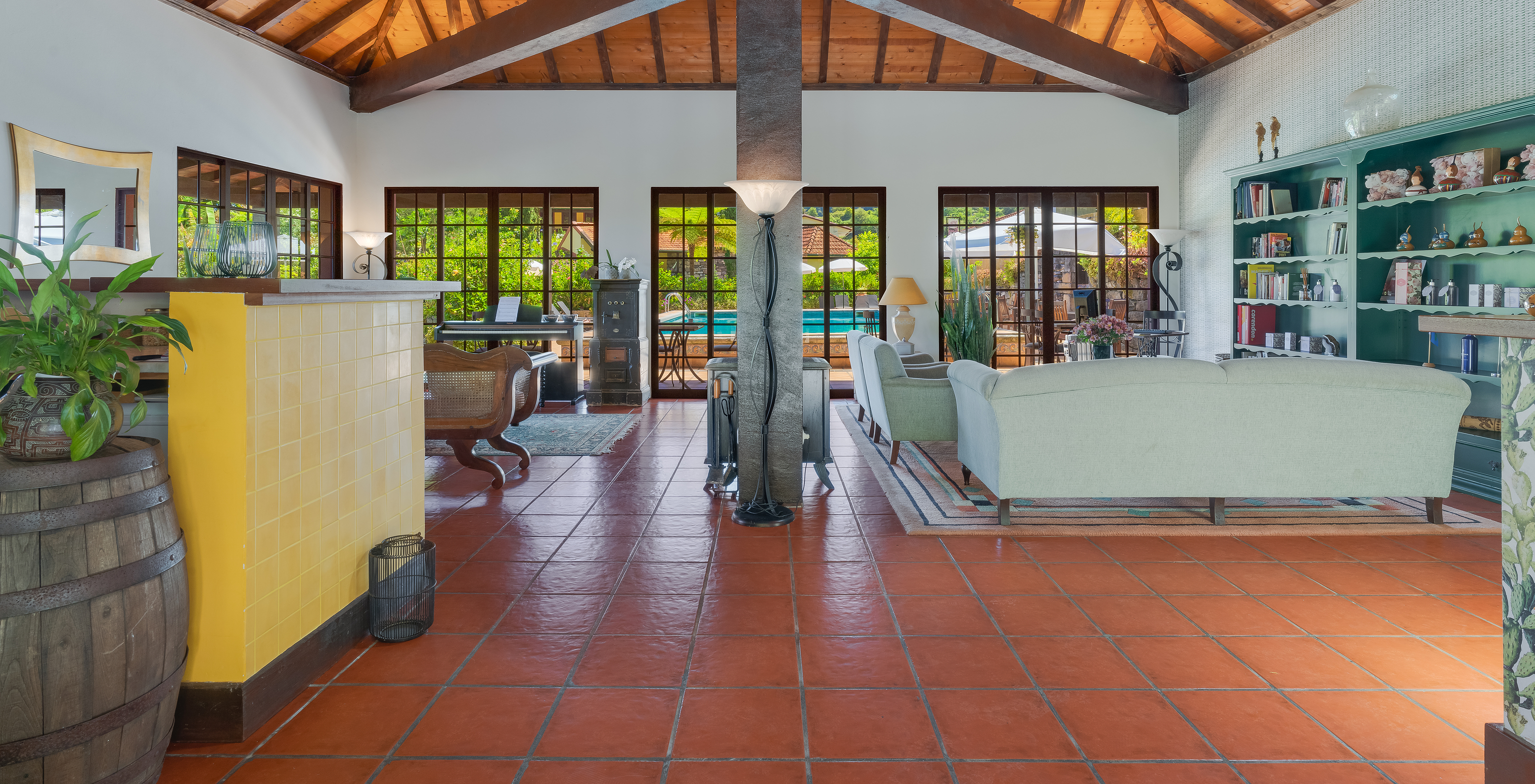 Hotel reception with desk, sofas, bookshelves, and glass doors overlooking the pool