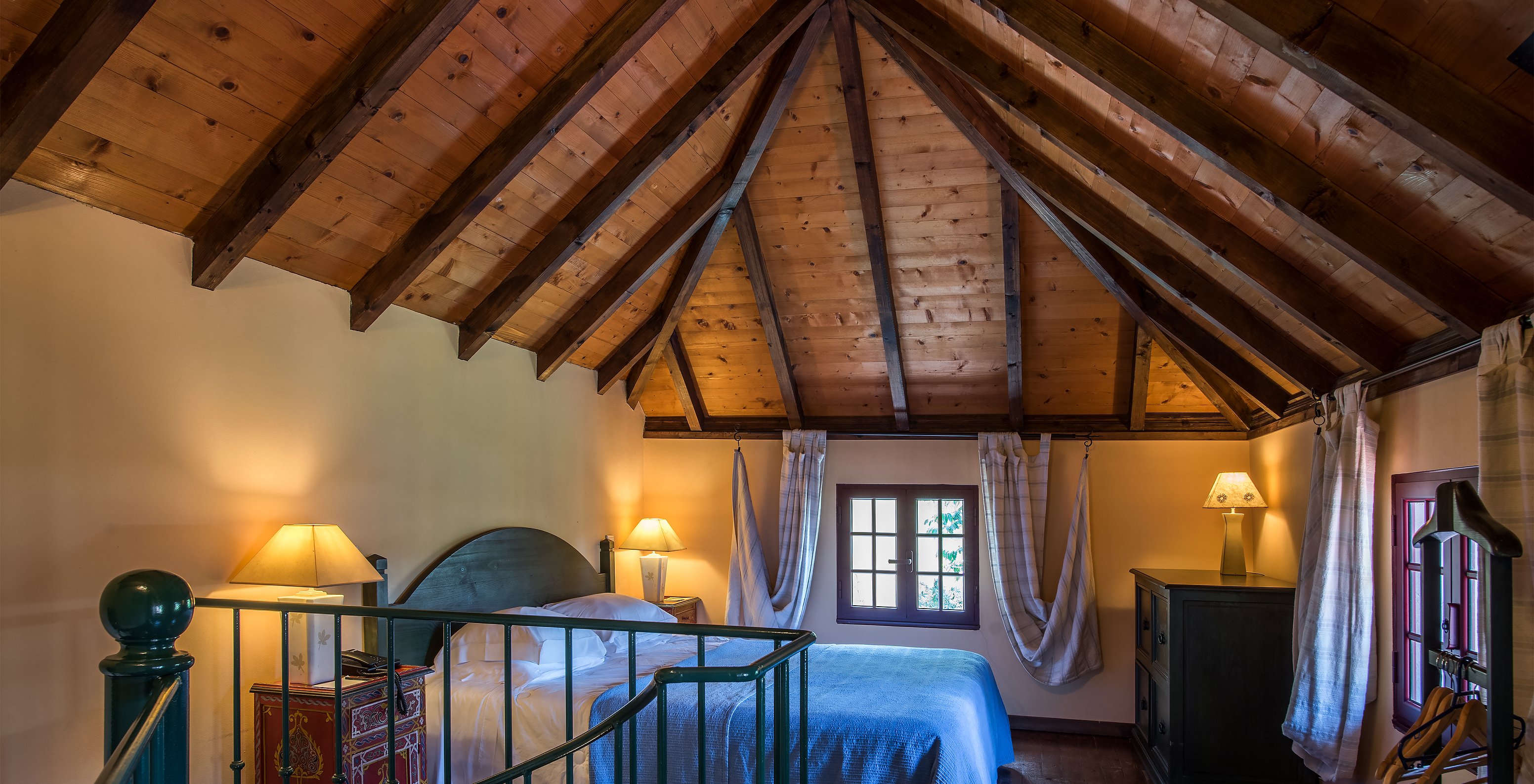 The Duplex Villas of Pestana Quinta do Arco have a double bed with wooden ceiling, nightstands, and wooden dresser