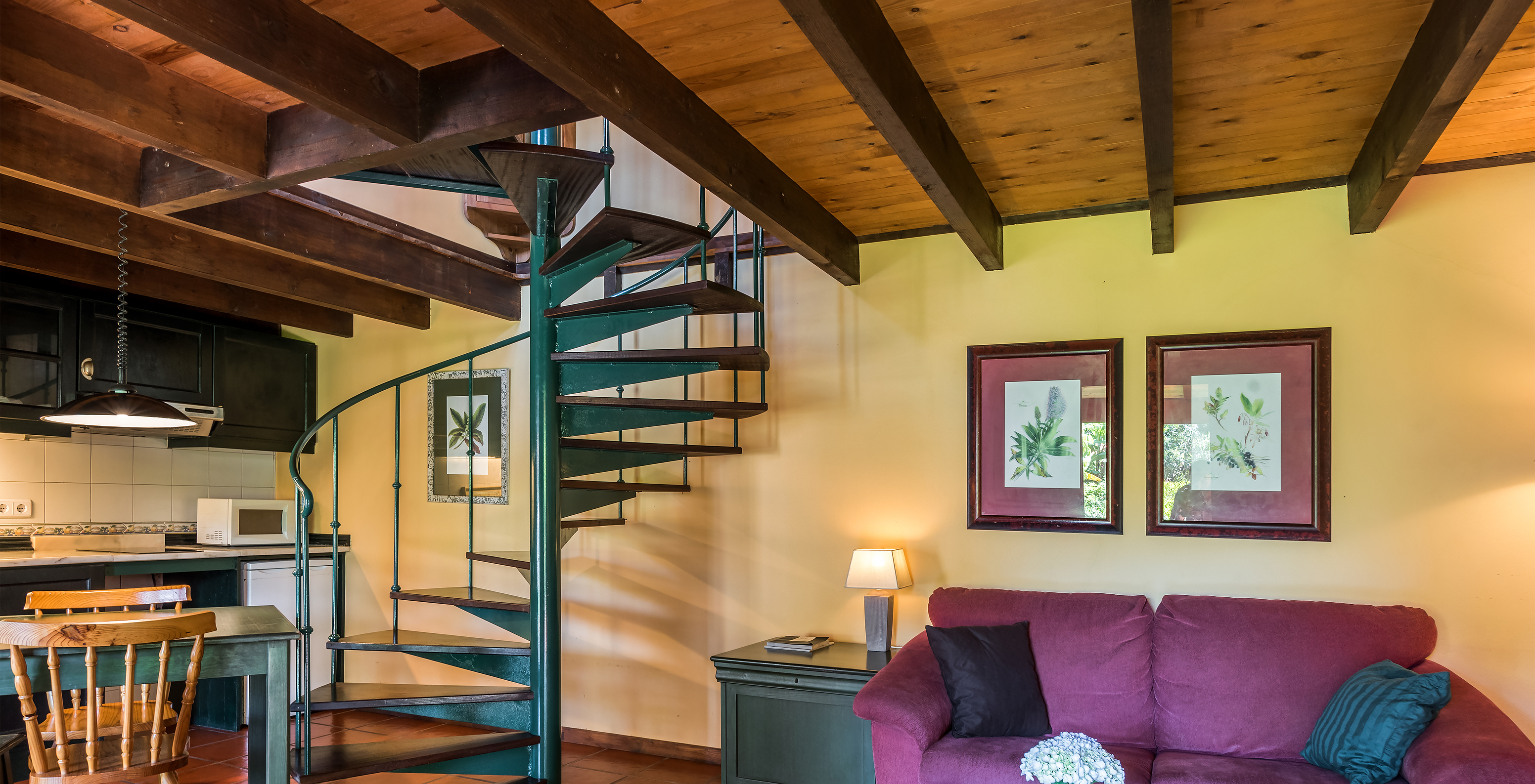 The Duplex Villas of Pestana Quinta do Arco have a sofa with a side table, kitchen, dining table, and metal stairs