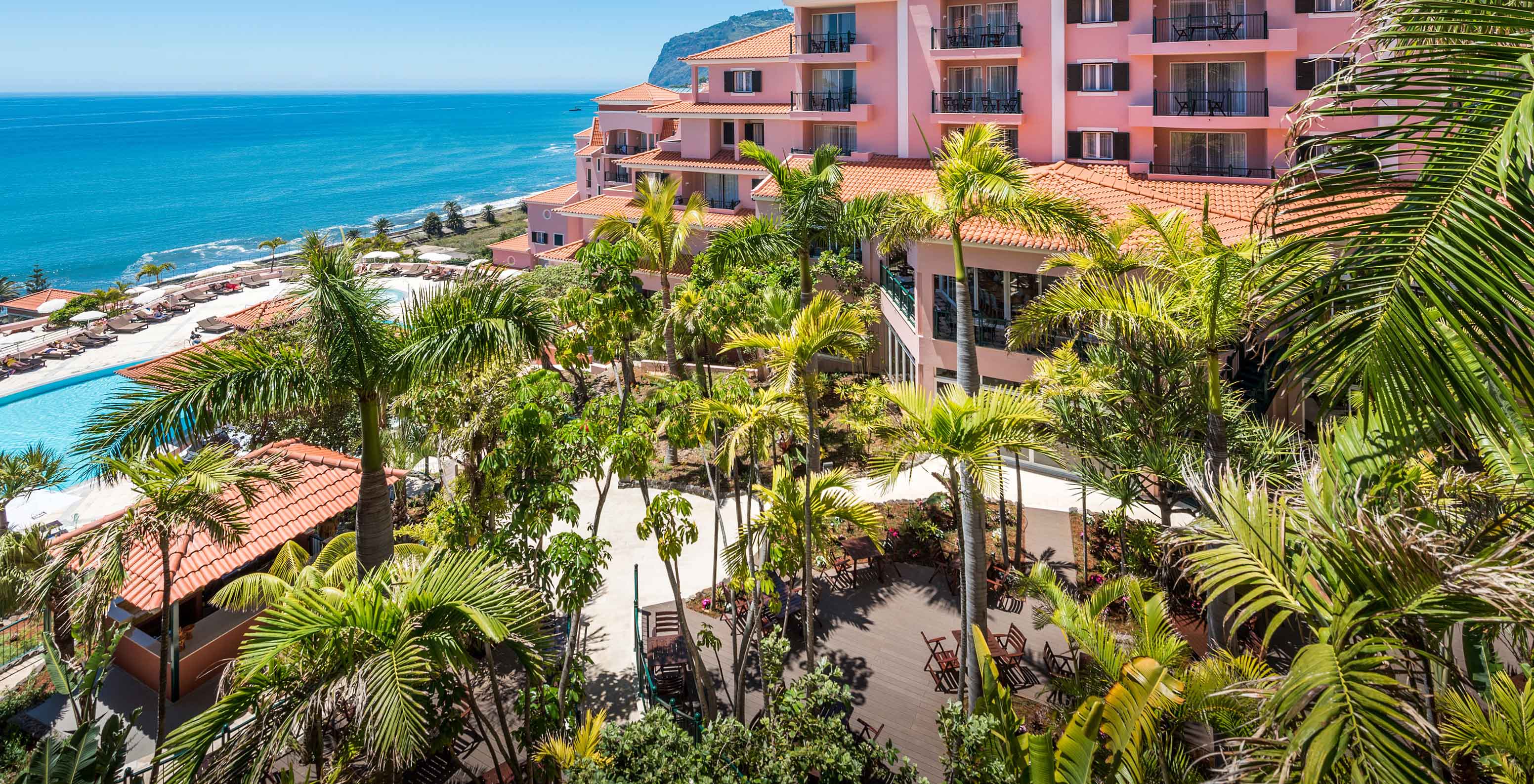 Landscape of Pestana Royal All Inclusive, with pink buildings, vegetation, and the ocean in the background