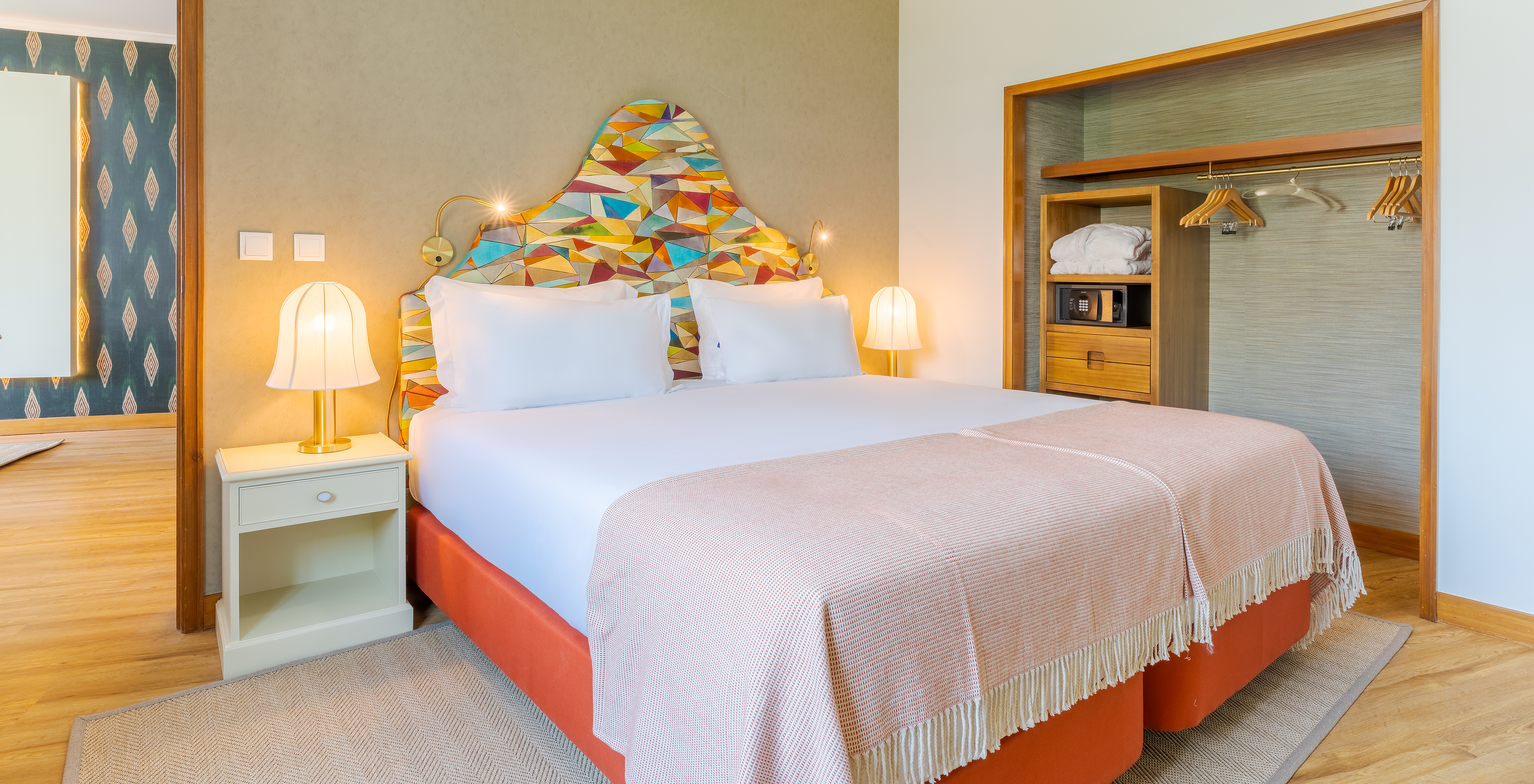 The Superior Lateral Sea View Suite at Pestana Vila Lido Madeira features a double bed with a colorful headboard and wardrobe