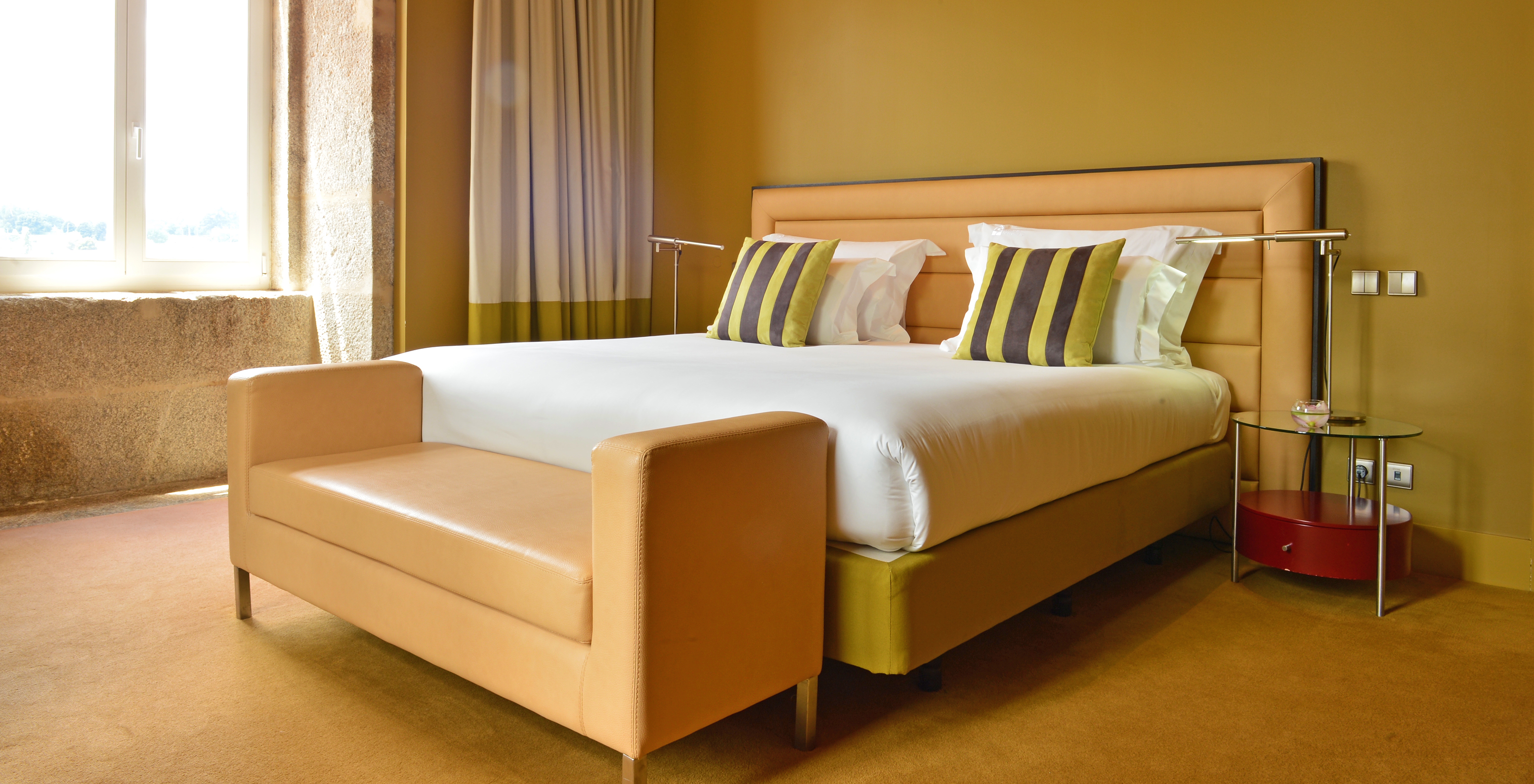 The Nasoni Suite of Pestana Palácio do Freixo has a double bed with a beige leather bench in the back and a window