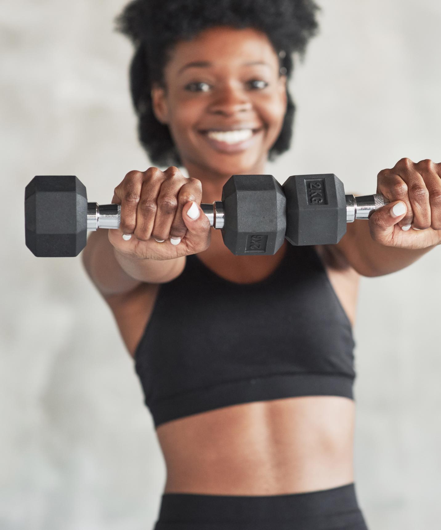 Smiling girl in workout clothes exercises with weights at a hotel with a pool, facing the beach