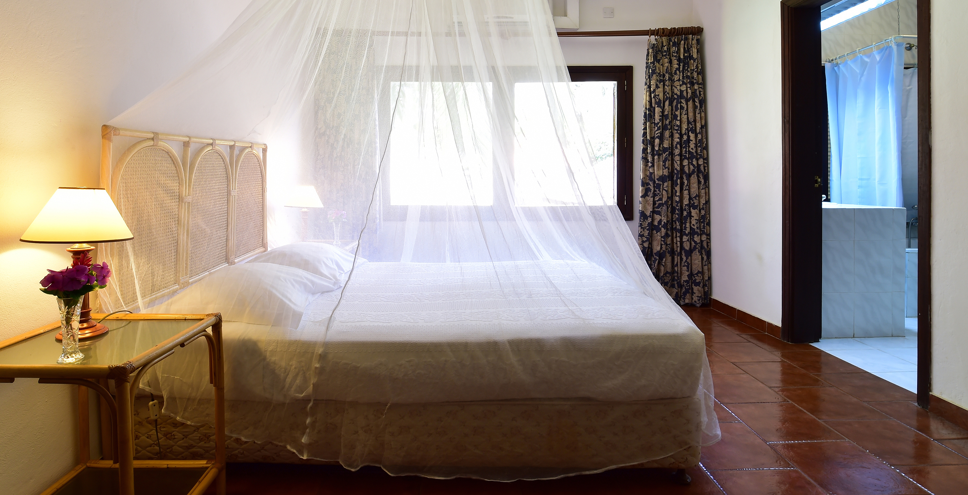 The Suite at Pestana Miramar São Tomé includes a double bed with a mosquito net, a bedside table, and a window