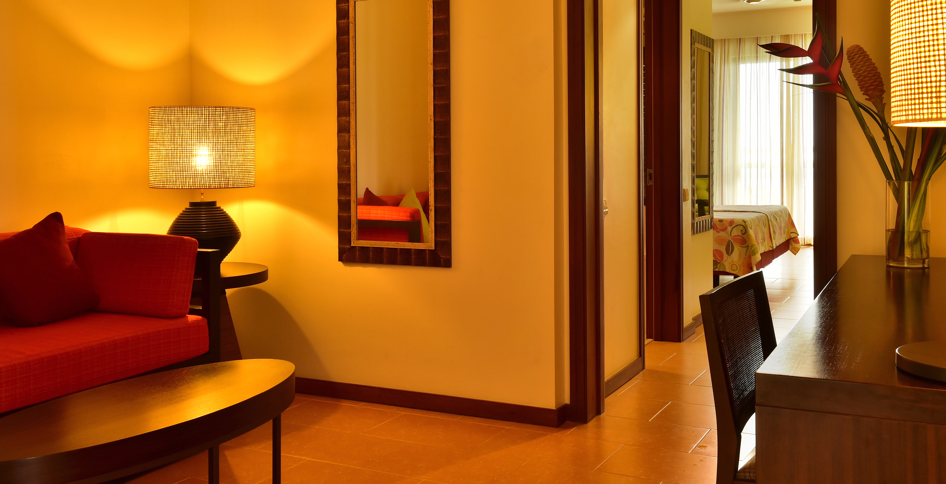 The Junior Suite of Pestana São Tomé has a room with a red sofa and a coffee table, and a desk with flowers decorating