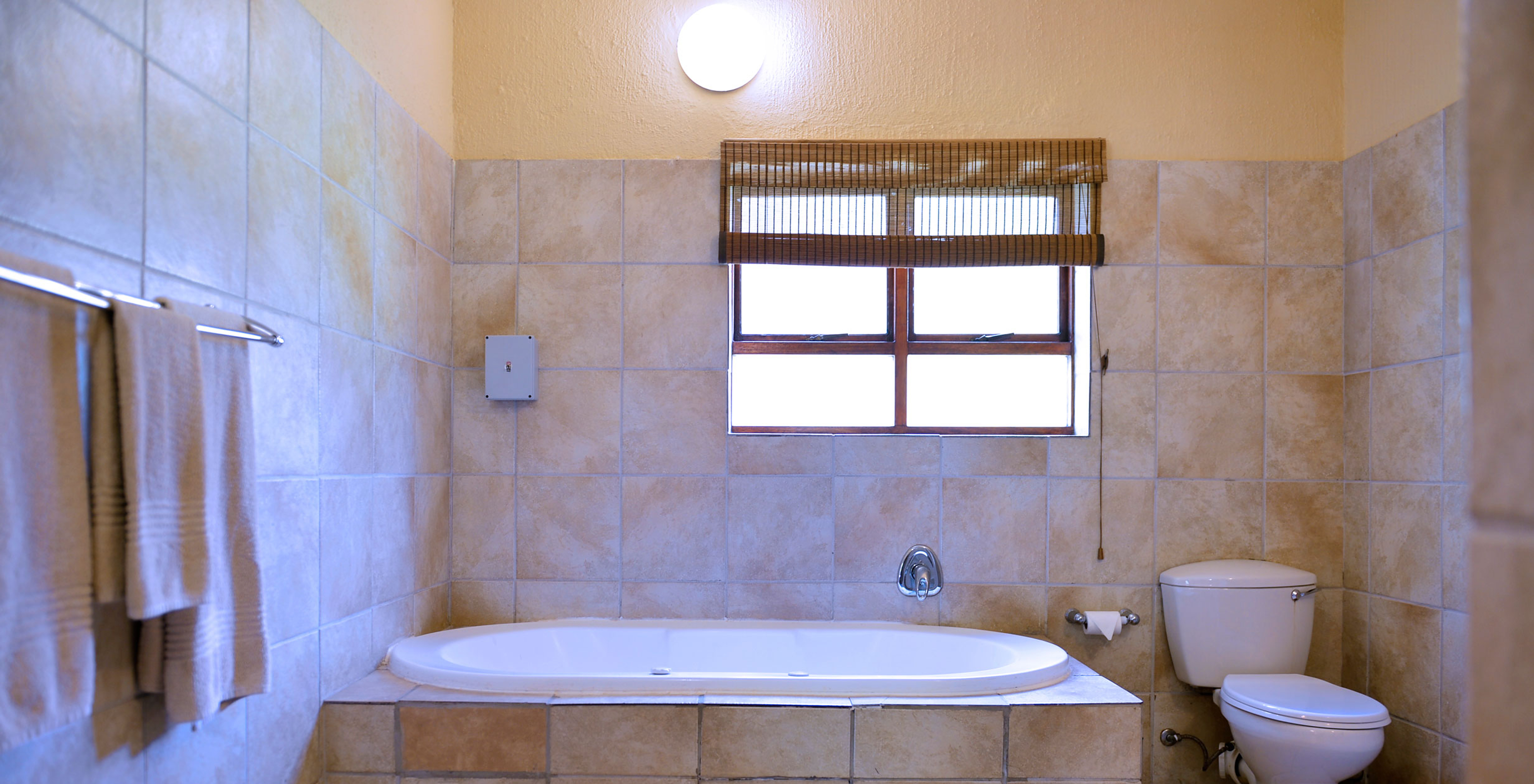 The Rhino Family Cottage at Pestana Kruger Lodge has a beige bathroom with a window, bathtub and toilet