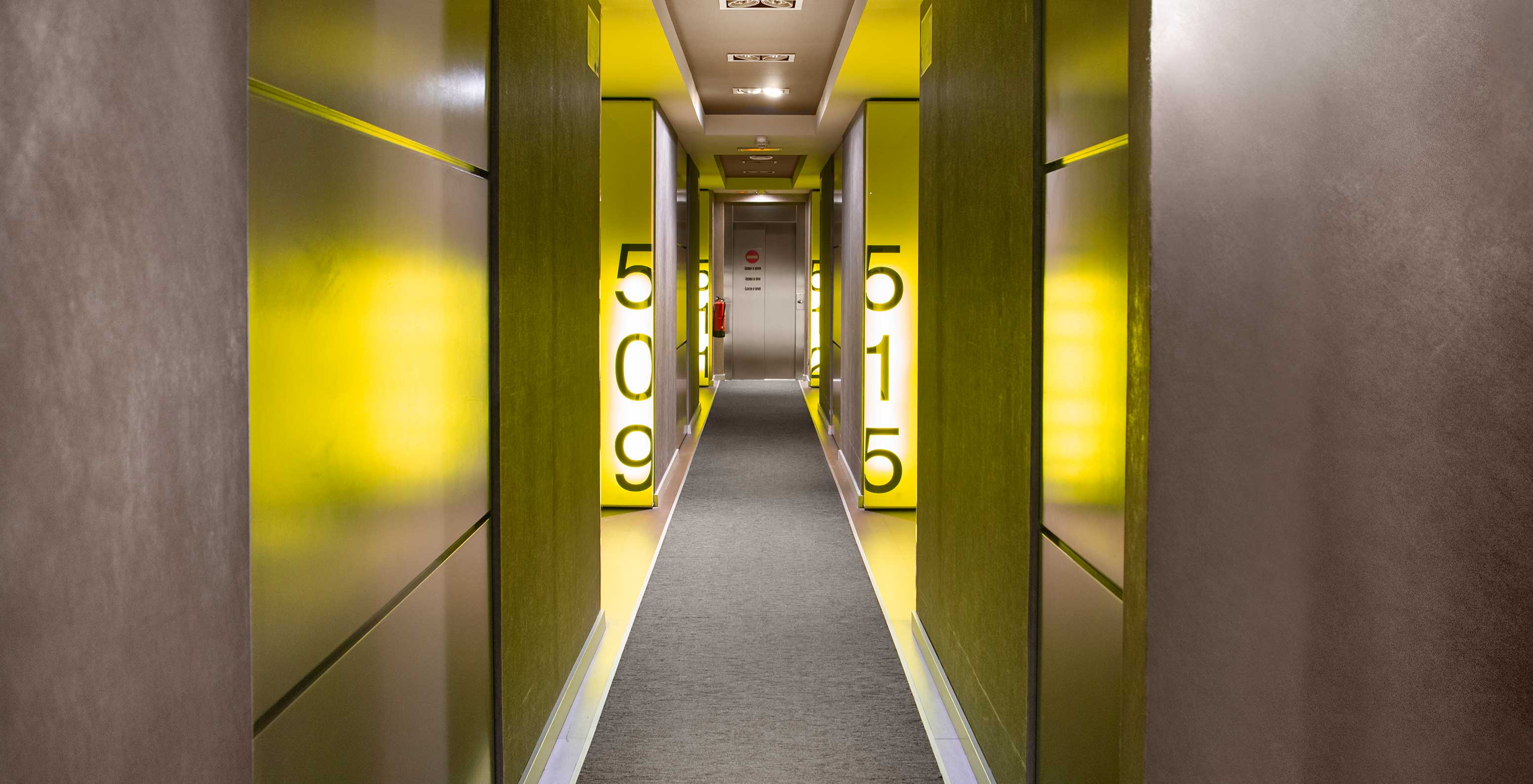 The hotel in Barcelona has a room hallway with a grey carpet, yellow lights, and visible room numbers