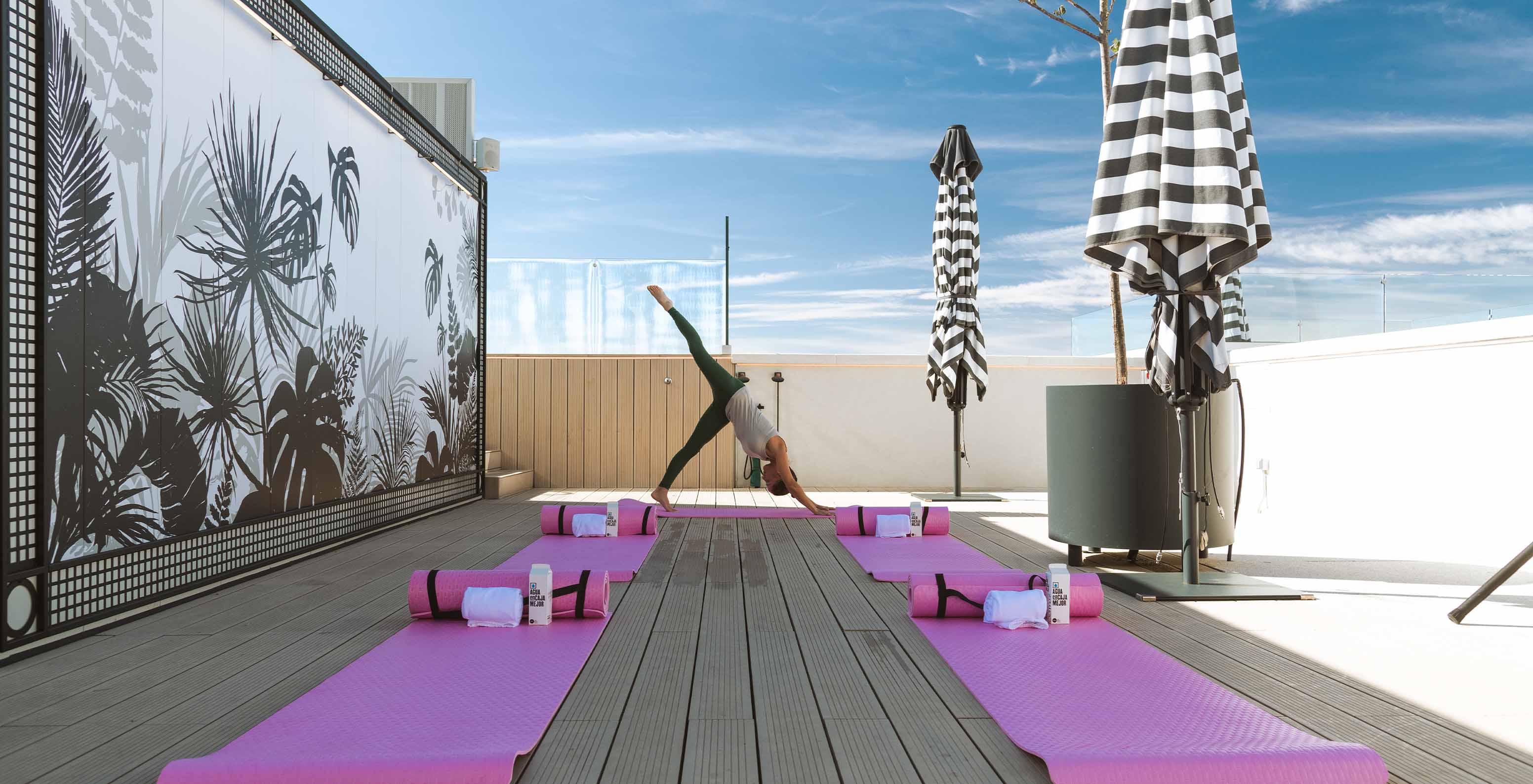 Girl practicing yoga on the hotel rooftop, with pink mats and sun umbrellas