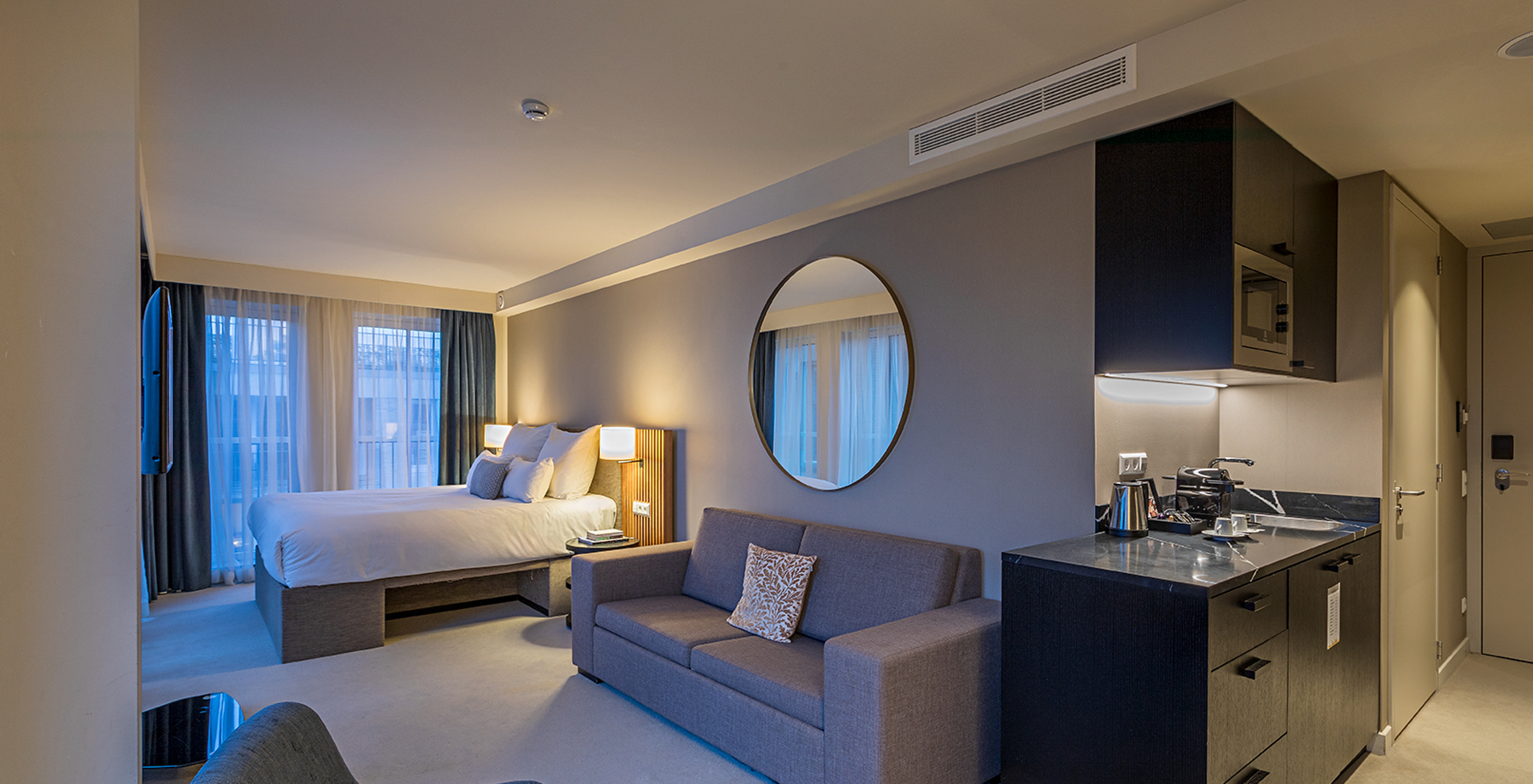 Premium Studio room at Pestana Amsterdam Riverside has a double bed, with gray sofa and a mirror above