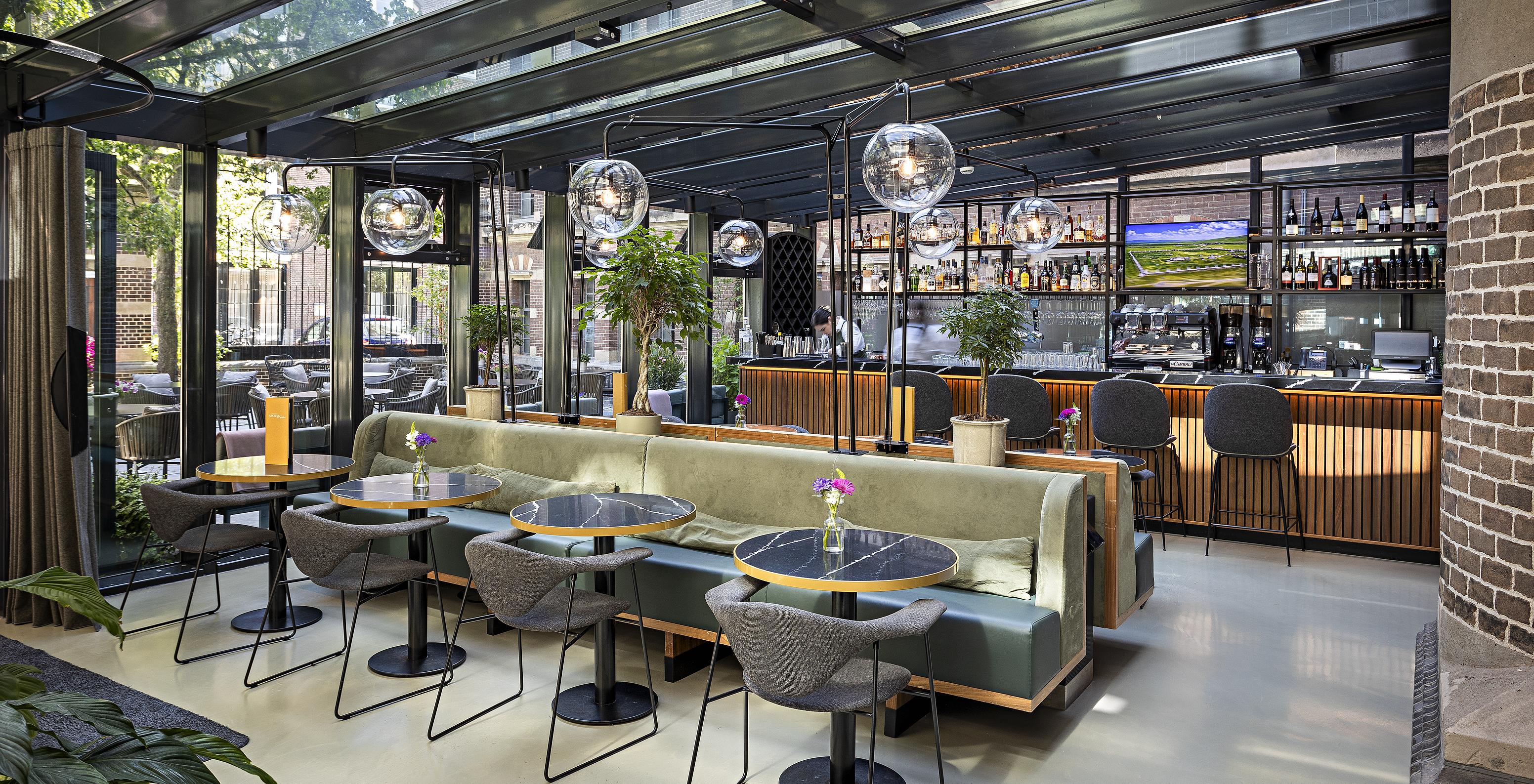 The Pestana Amsterdam Riverside has a restaurant with tables and sofas and a glass structure