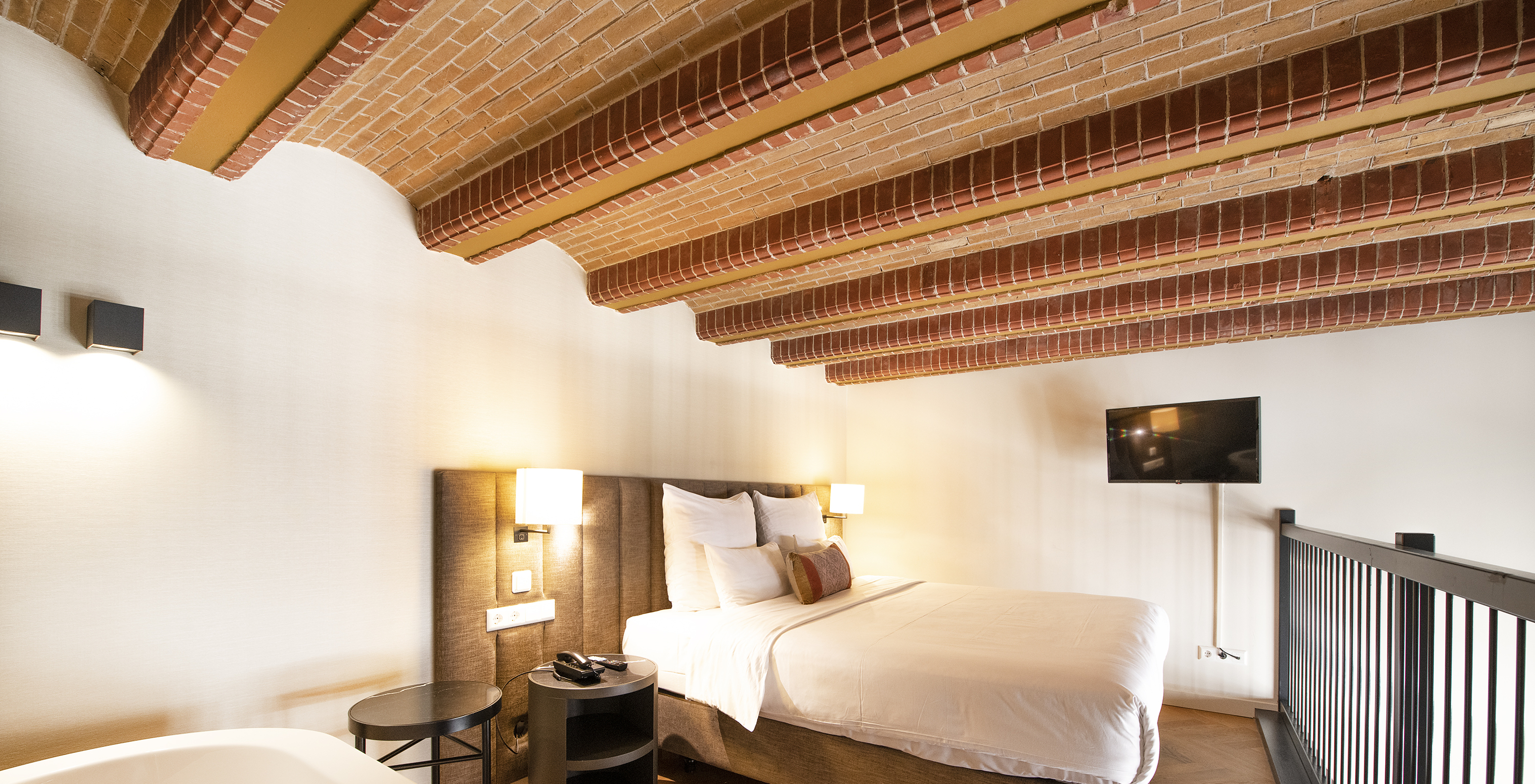 Mezzanine Suite at Pestana Amsterdam Riverside has a double bed, with bedside table, and red brick ceiling