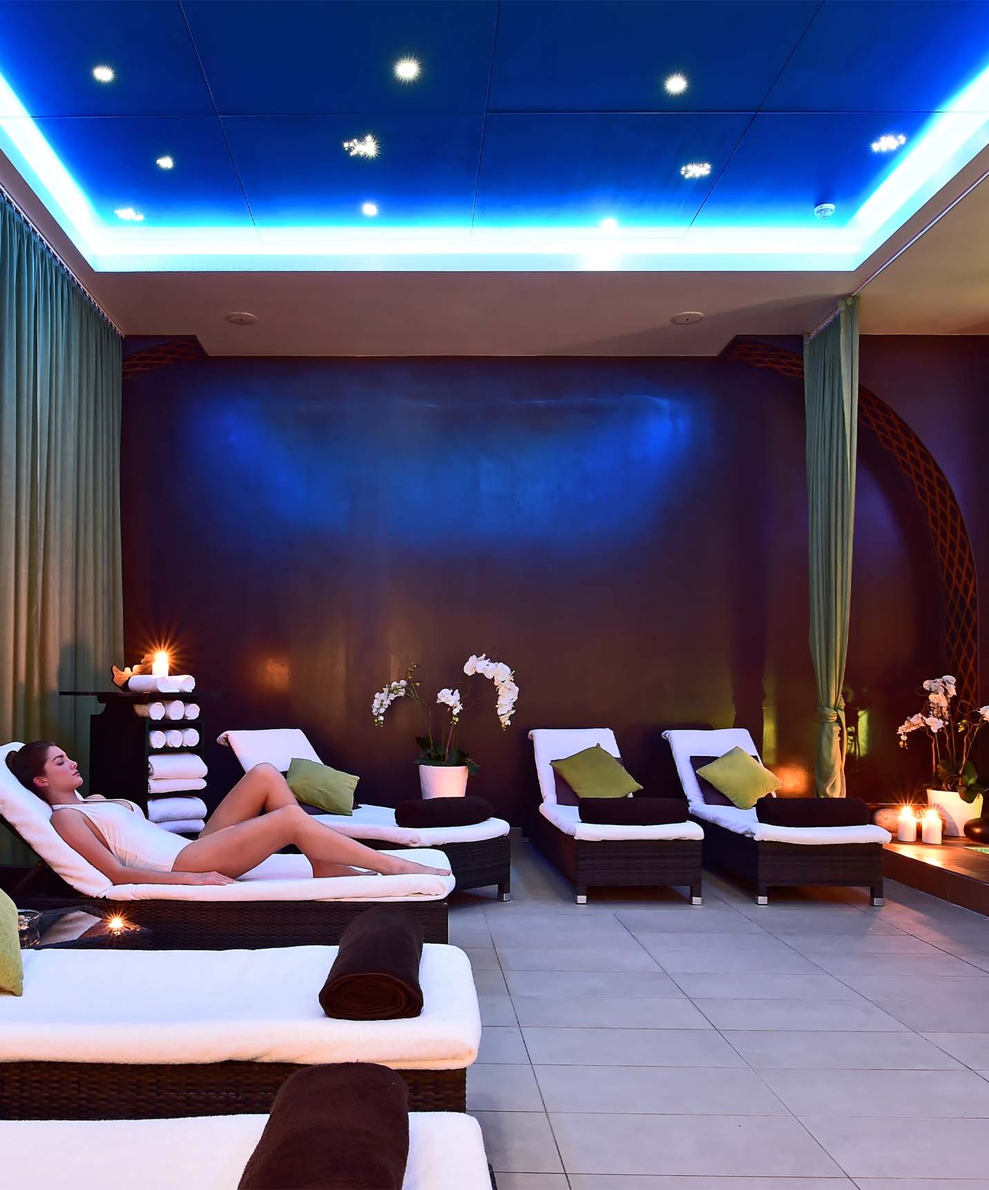 Indoor pool of the hotel with loungers with white mattresses, with a lady relaxing and blue lights