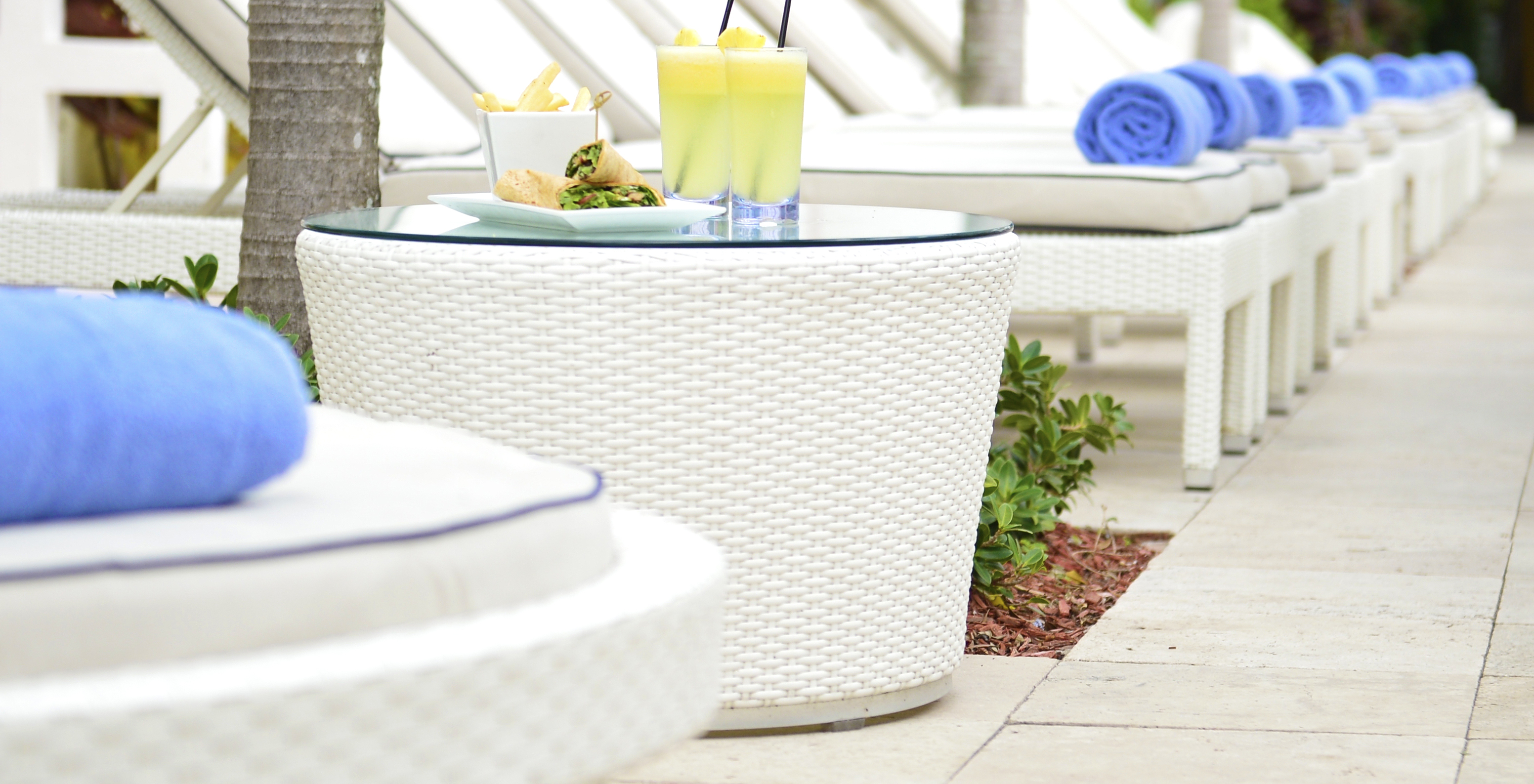 Outdoor bar area with white loungers, coffee tables, and two cocktails, wraps, and potato sticks