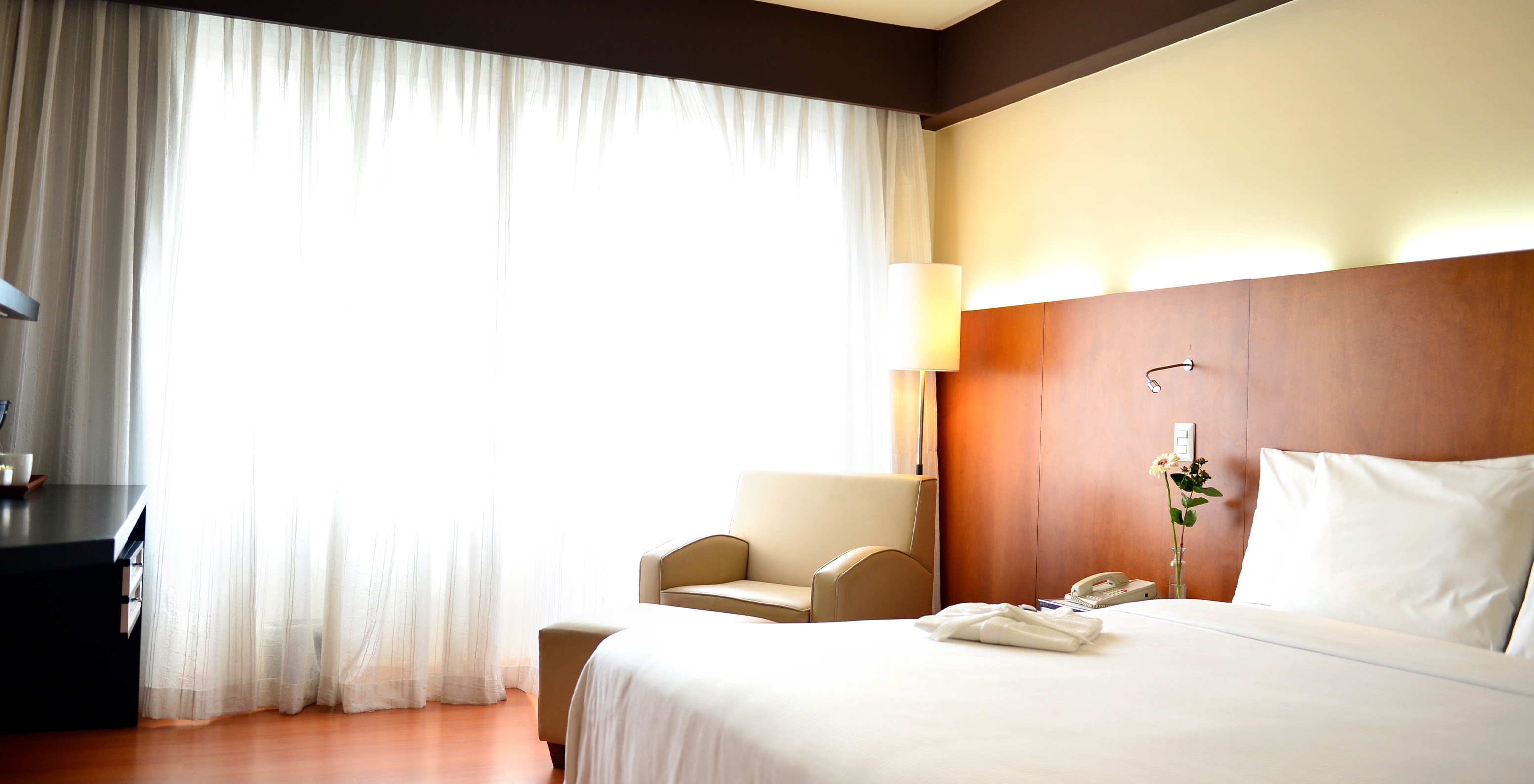 The Executive King Room at Pestana Caracas has a double bed with a wooden headboard and a window with curtains