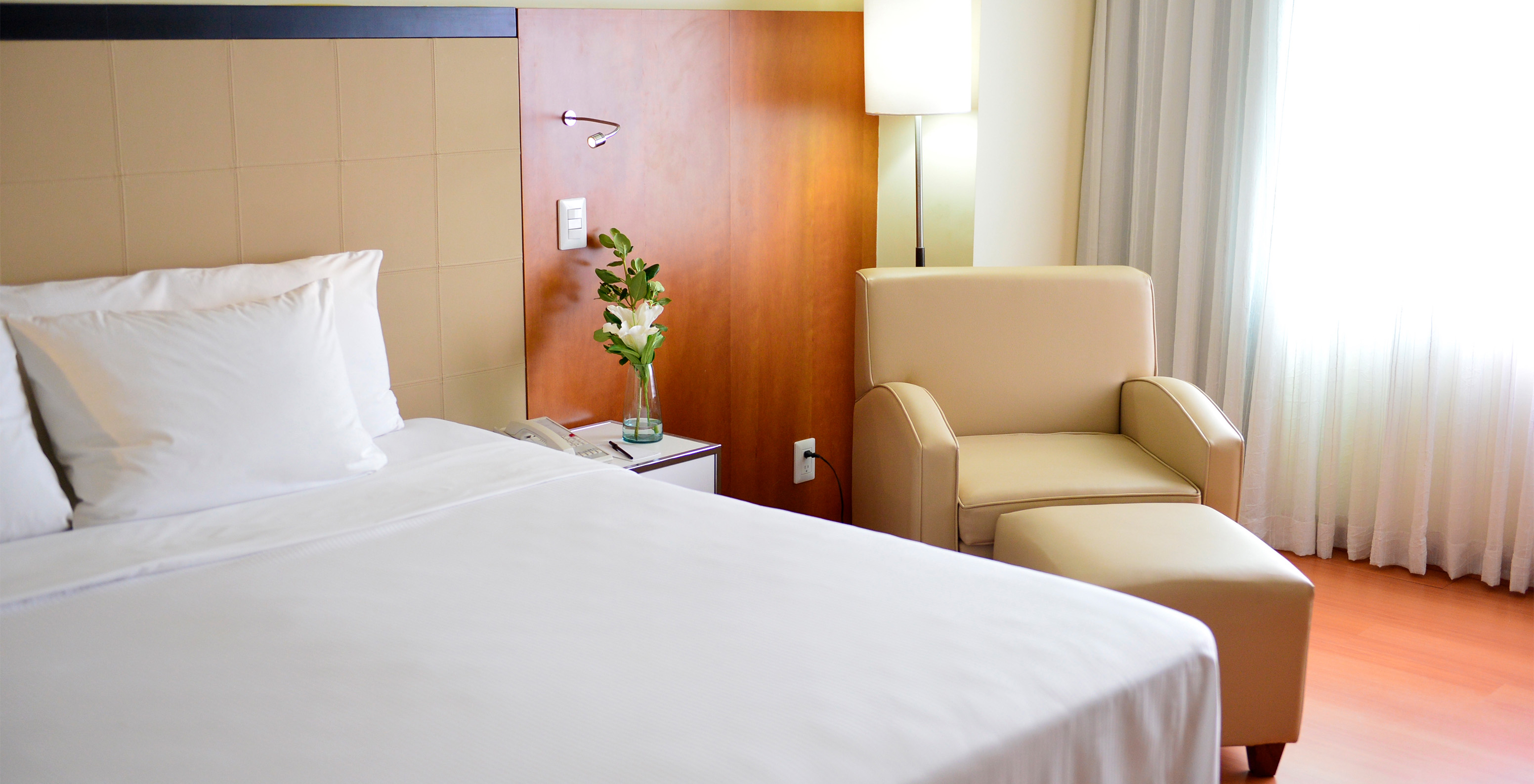 The Twin Executive Room at Pestana Caracas has a double bed, a flower on the bedside table, and a comfortable beige armchair