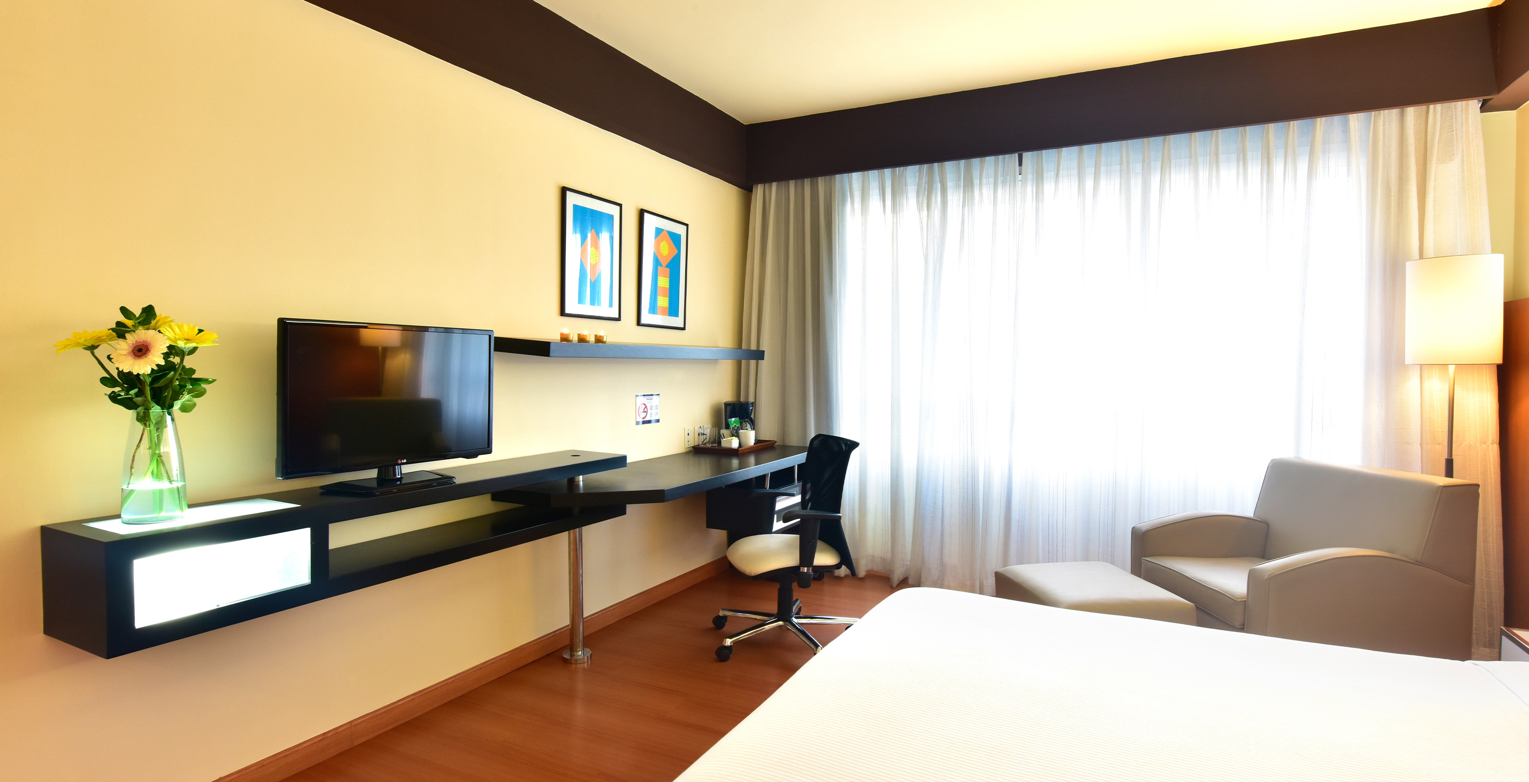 The Twin Superior Room at Pestana Caracas has a TV at the end of the bed, an armchair, a desk, and a window