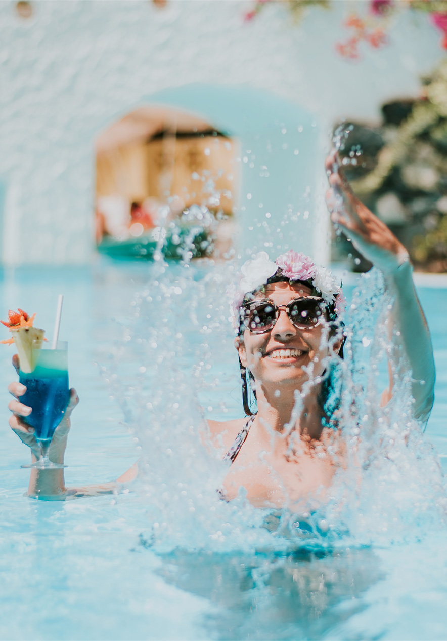 Enjoy the all-inclusive package at Pestana Hotels and Resorts Happy woman playing with water, holding a cocktail, enjoying the all-inclusive package without worries