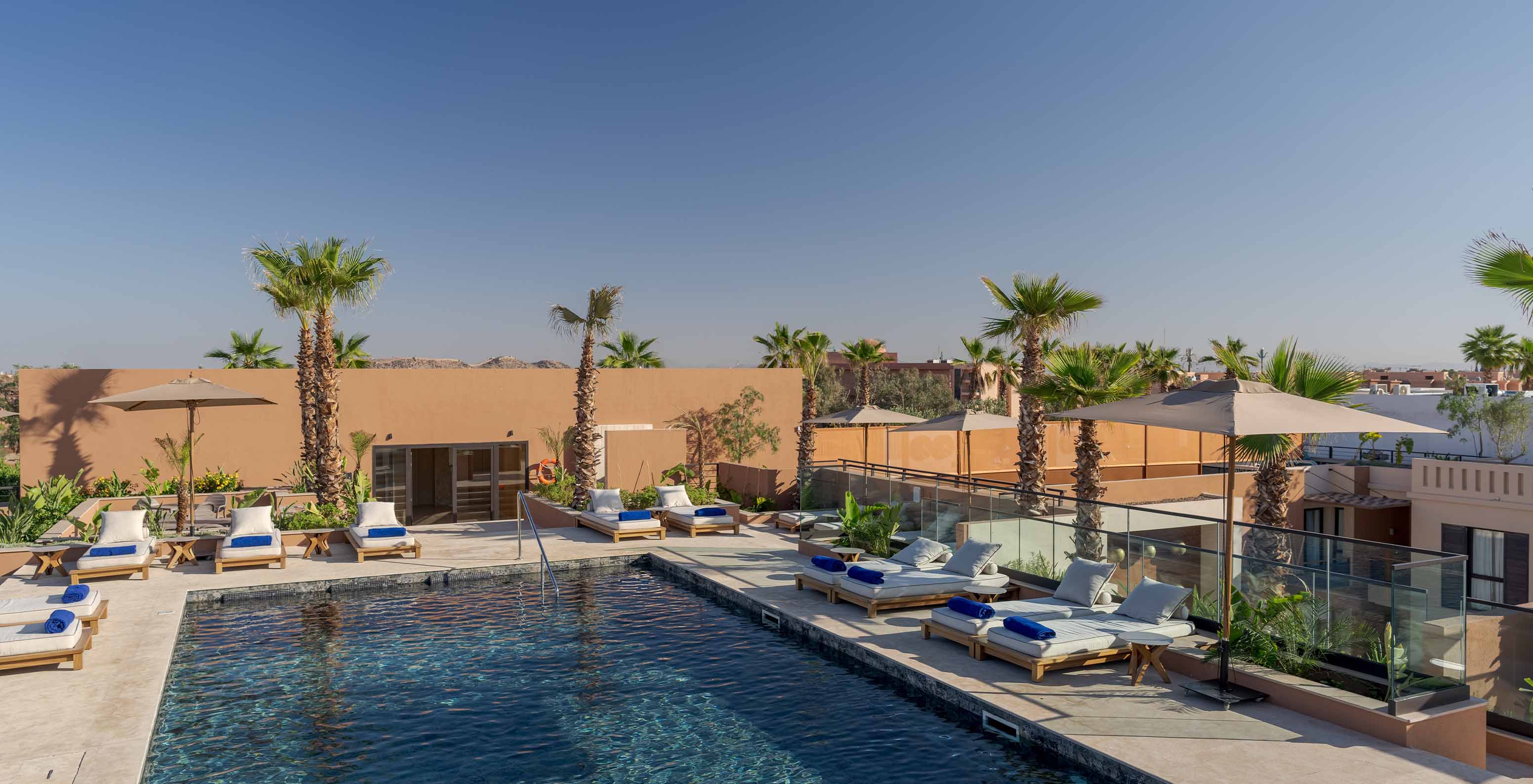 La piscina exterior en el rooftop del hotel lifestyle en Marruecos con varias tumbonas con almohadas y vista sobre la ciudad