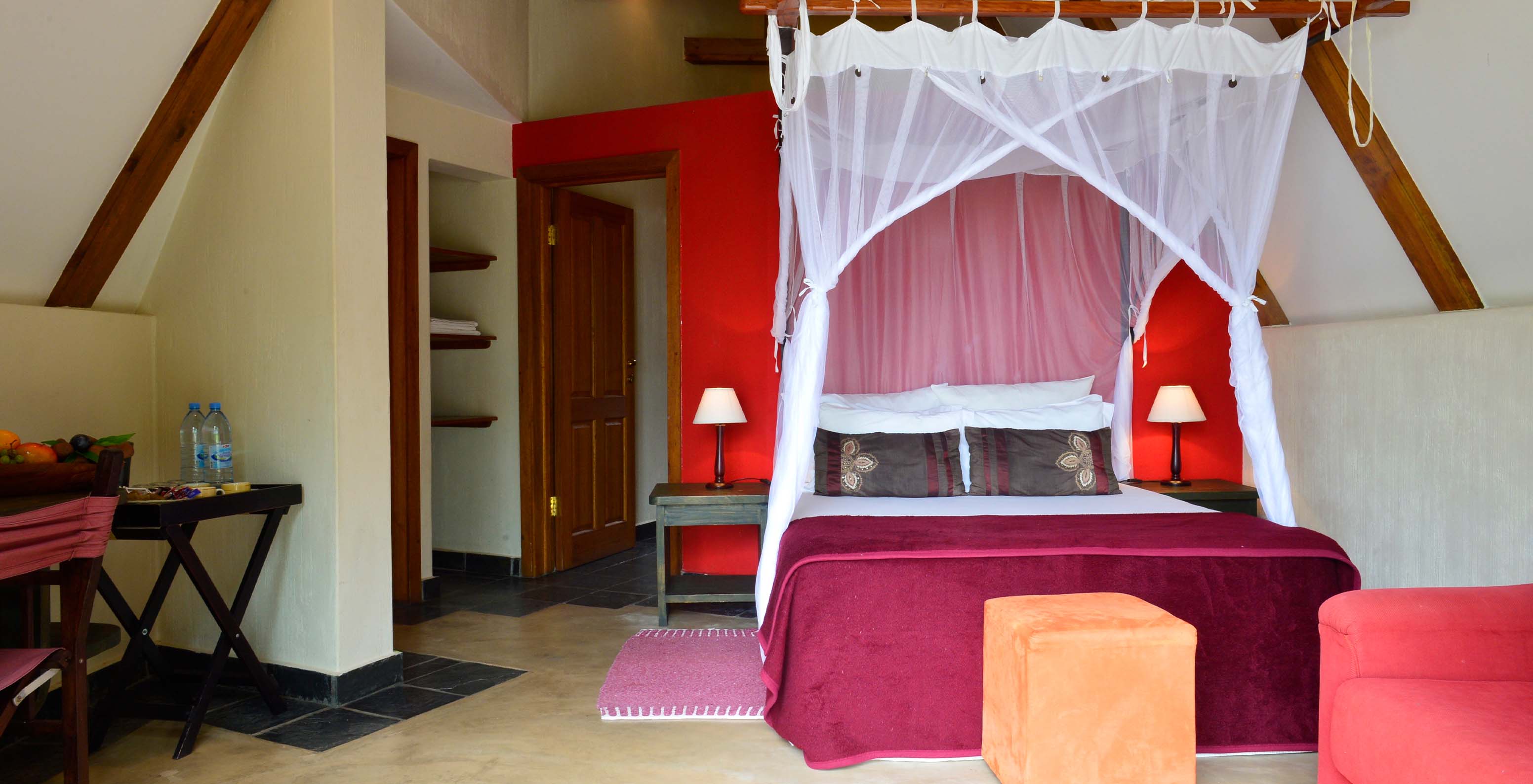 El Bungalow T1 del Pestana Bazaruto Lodge tiene decoración en tonos rojos con cama doble, sofá y escritorio