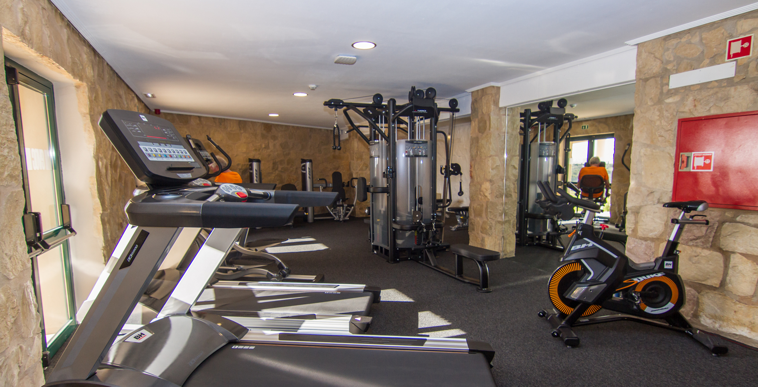 Gimnasio de hotel con piscina, ubicado en un campo de golf, con varias máquinas como cinta y bicicleta