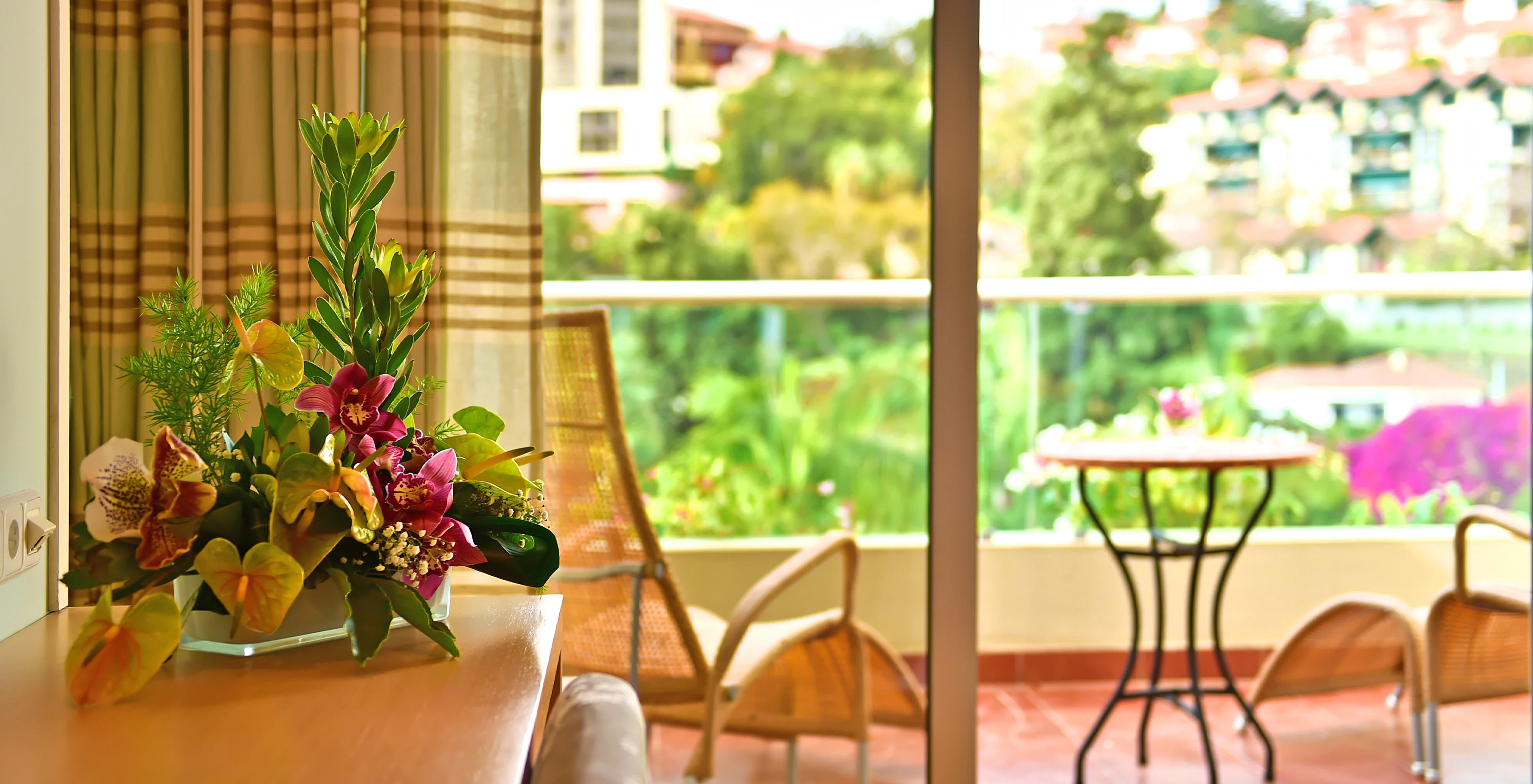 La habitación Doble Clásica Vista Piscina del Pestana Carlton Madeira tiene cómoda con flores y una terraza con mesa y sillas