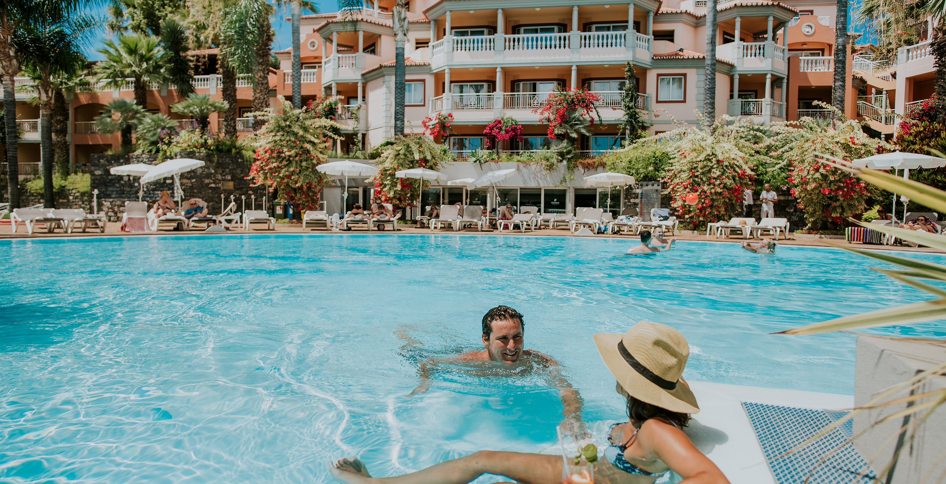 Pareja en la piscina, conversando y bebiendo cócteles, en el Pestana Miramar, un hotel en Madeira cerca de la playa