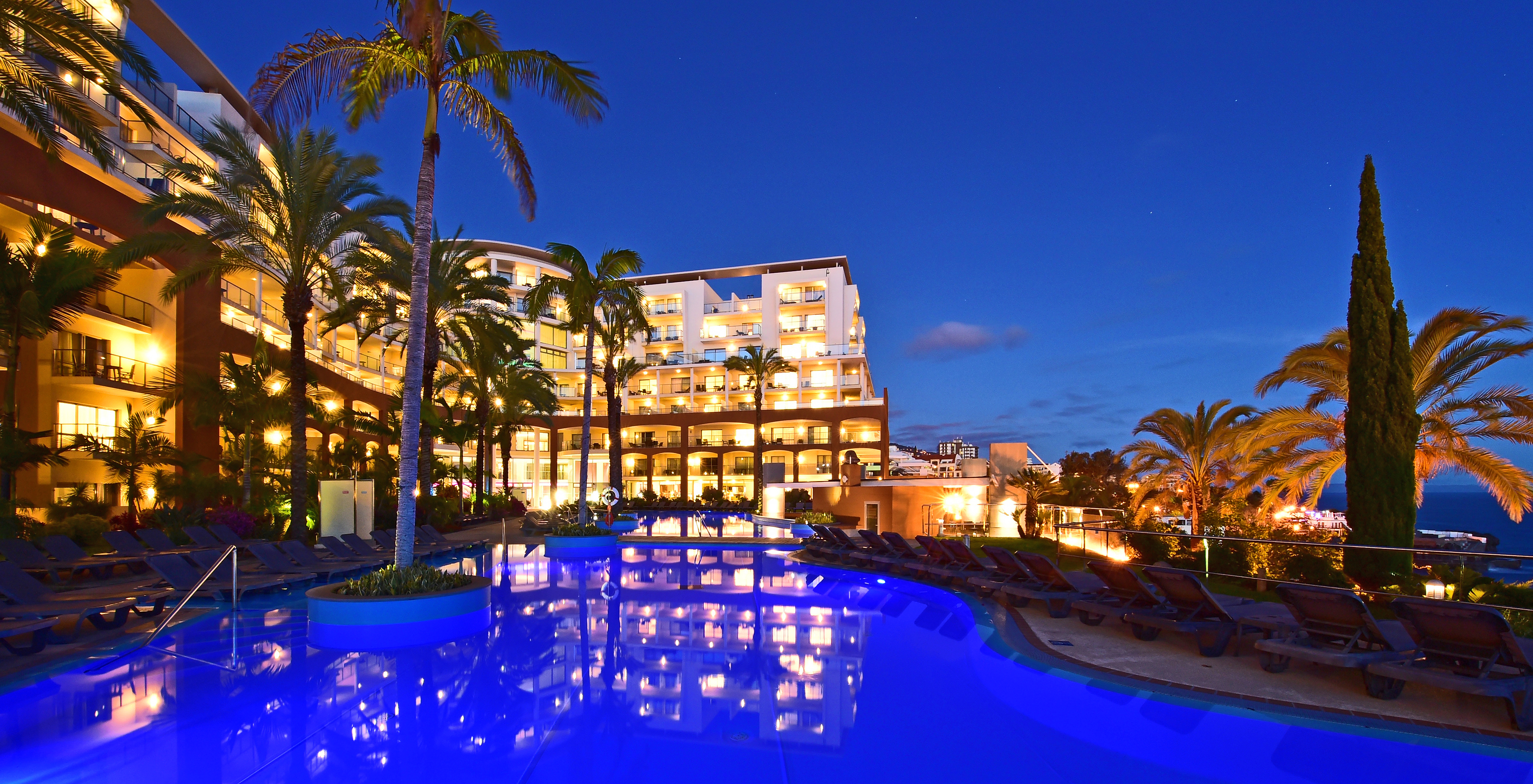 Vista nocturna de la piscina del Pestana Promenade, iluminada y con el edificio del hotel iluminado al fondo