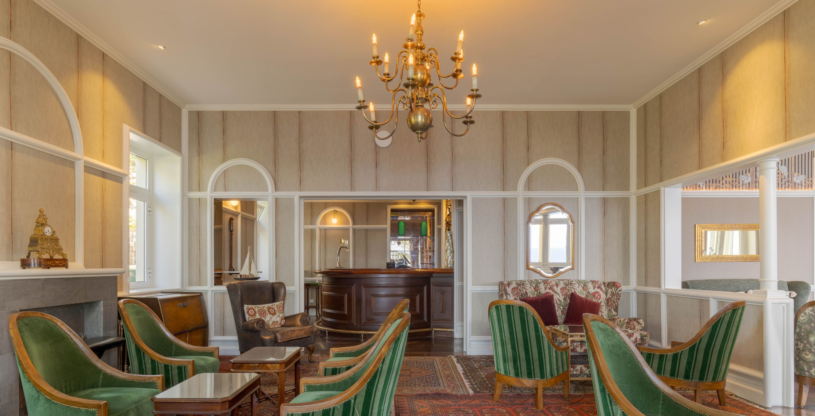 El Bar Vila Lido, del Hotel con Acceso al Mar en Funchal, tiene una zona de estar con mesas de madera y vidrio y sillones verdes.