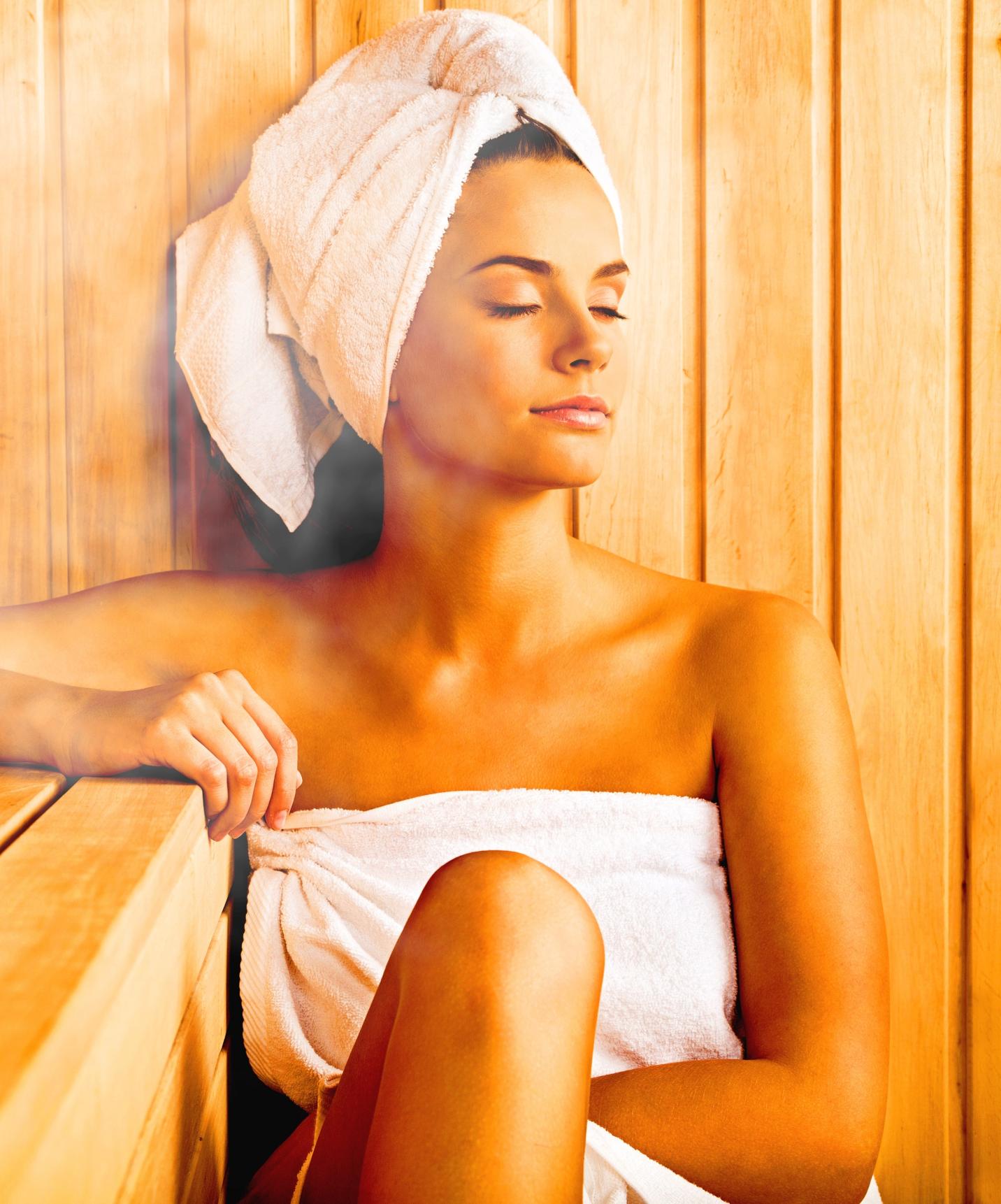 Chica con toalla sonriente y con los ojos cerrados se relaja en la sauna de hotel con piscina, frente a la playa